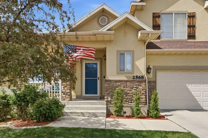 Stucco exterior with stone veneer accents, an attached garage, covered porch, and mature landscaping