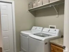 Dedicated laundry area featuring a white paneled door, wood-finish flooring, a wall-mounted shelving unit, and a built-in wood-finish cabinet with a neutral countertop