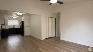 Open-concept living space with wood-finish flooring, a ceiling fan, and white walls