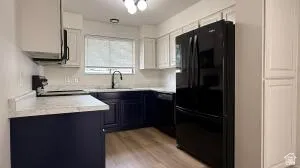 Modern kitchen featuring two-tone cabinetry, white countertops, a black appliance suite, and wood-finish flooring
