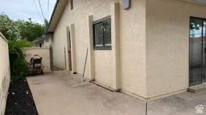 Exterior patio featuring a neutral stucco finish, dark-trimmed window with blinds, and a sliding glass door