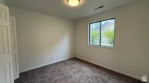 Interior room featuring neutral wall paint, dark patterned carpet, a single window with dark framing, and a flush-mount ceiling light fixture