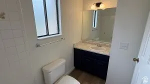 Bathroom featuring a vanity with a white countertop and dark cabinetry, a wall-mounted mirror, overhead lighting, a single window, and light wood-finish flooring