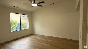 Spacious room featuring wood-finish flooring, a large window, a ceiling fan, and vaulted ceilings