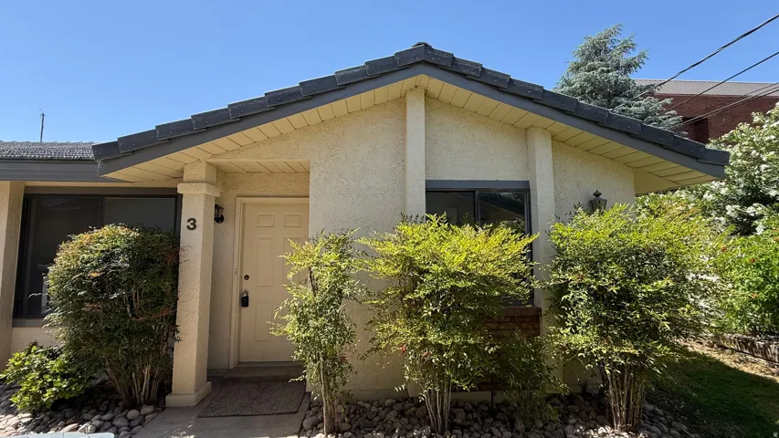 Entryway featuring a light stucco exterior, dark tile roof, a solid front door, and established landscaping with decorative rock accents