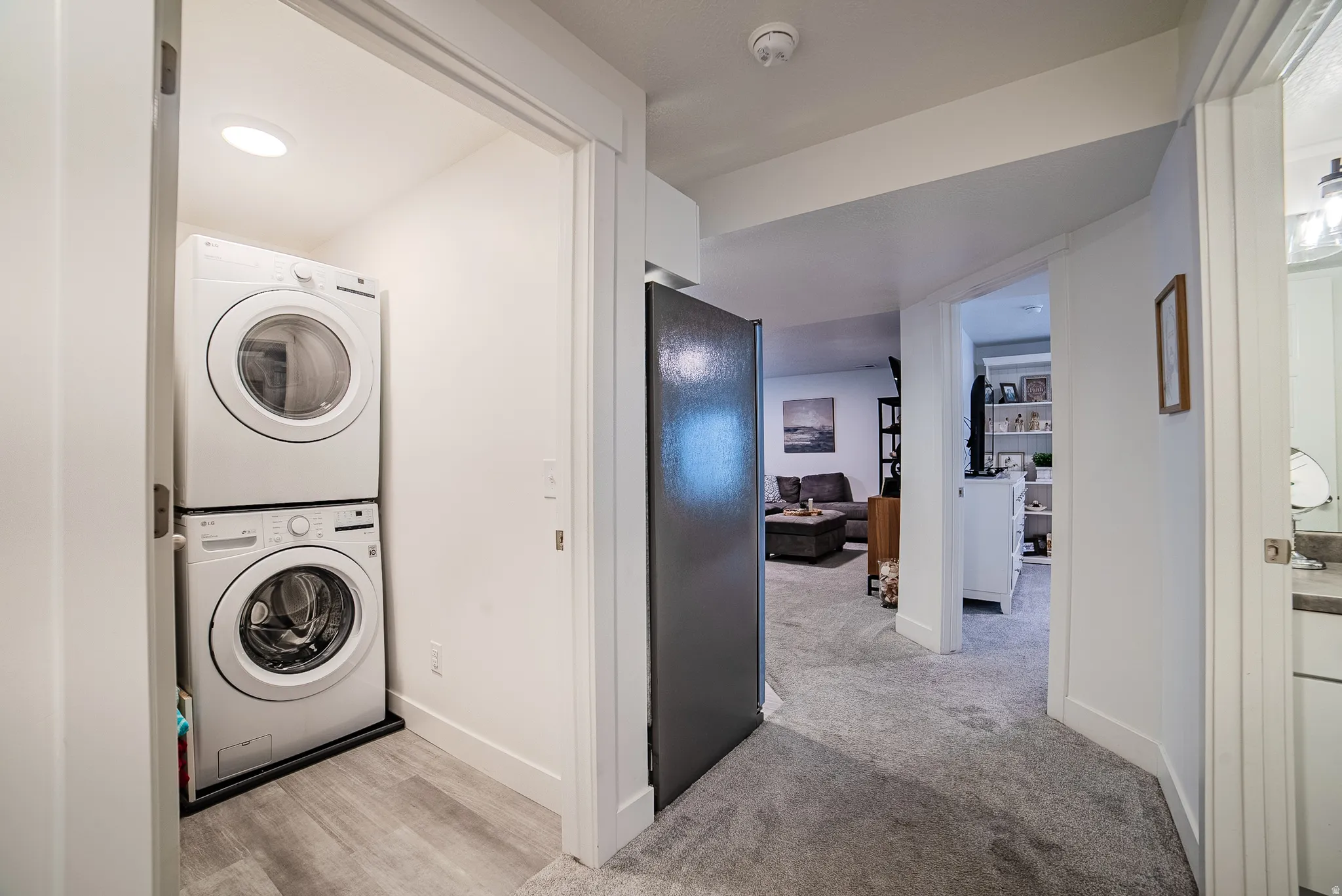 Dedicated laundry area featuring a stacked washer and dryer unit, recessed lighting, and wood-finish flooring
