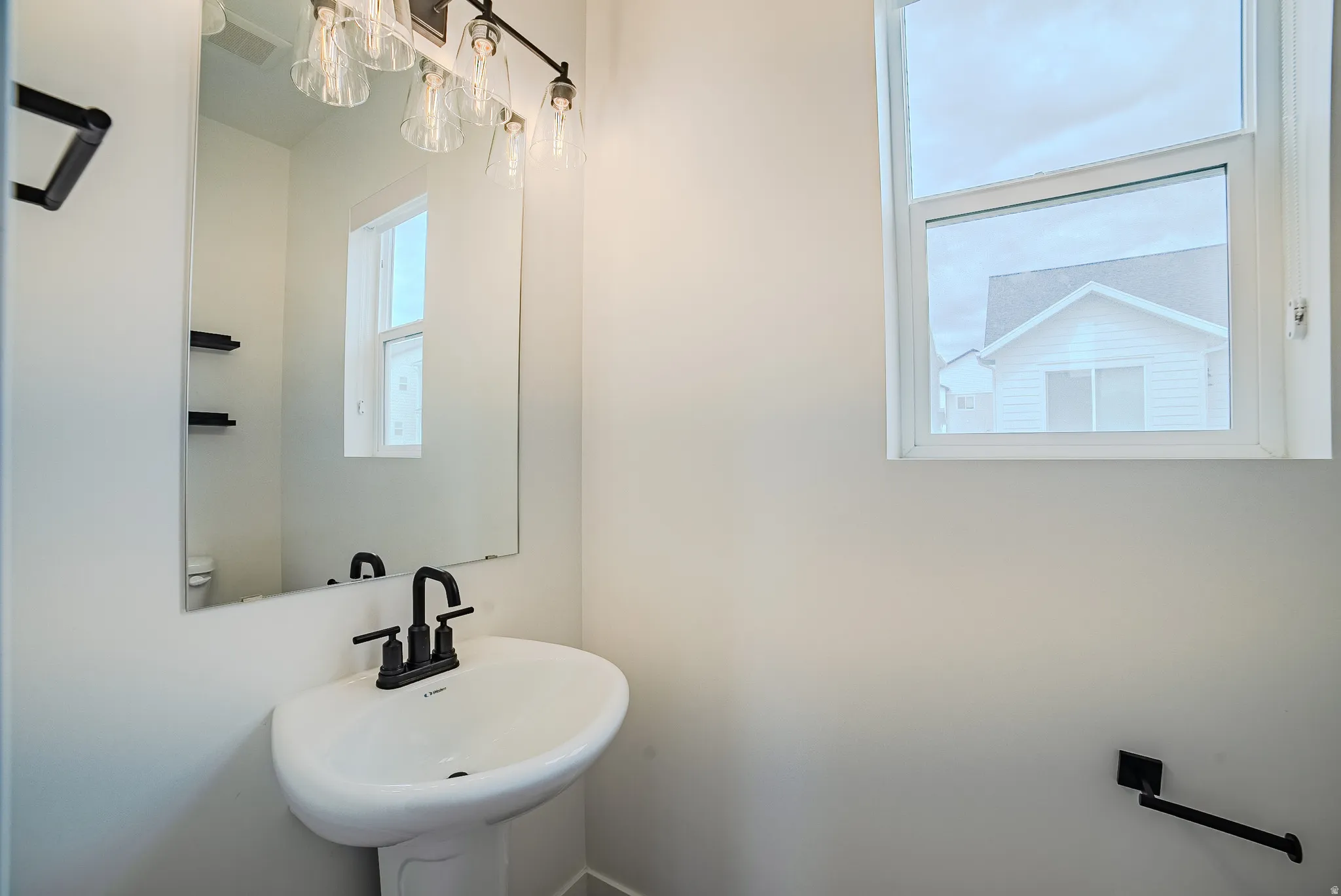 Pedestal sink with a matte black faucet, illuminated by a multi-bulb vanity light fixture