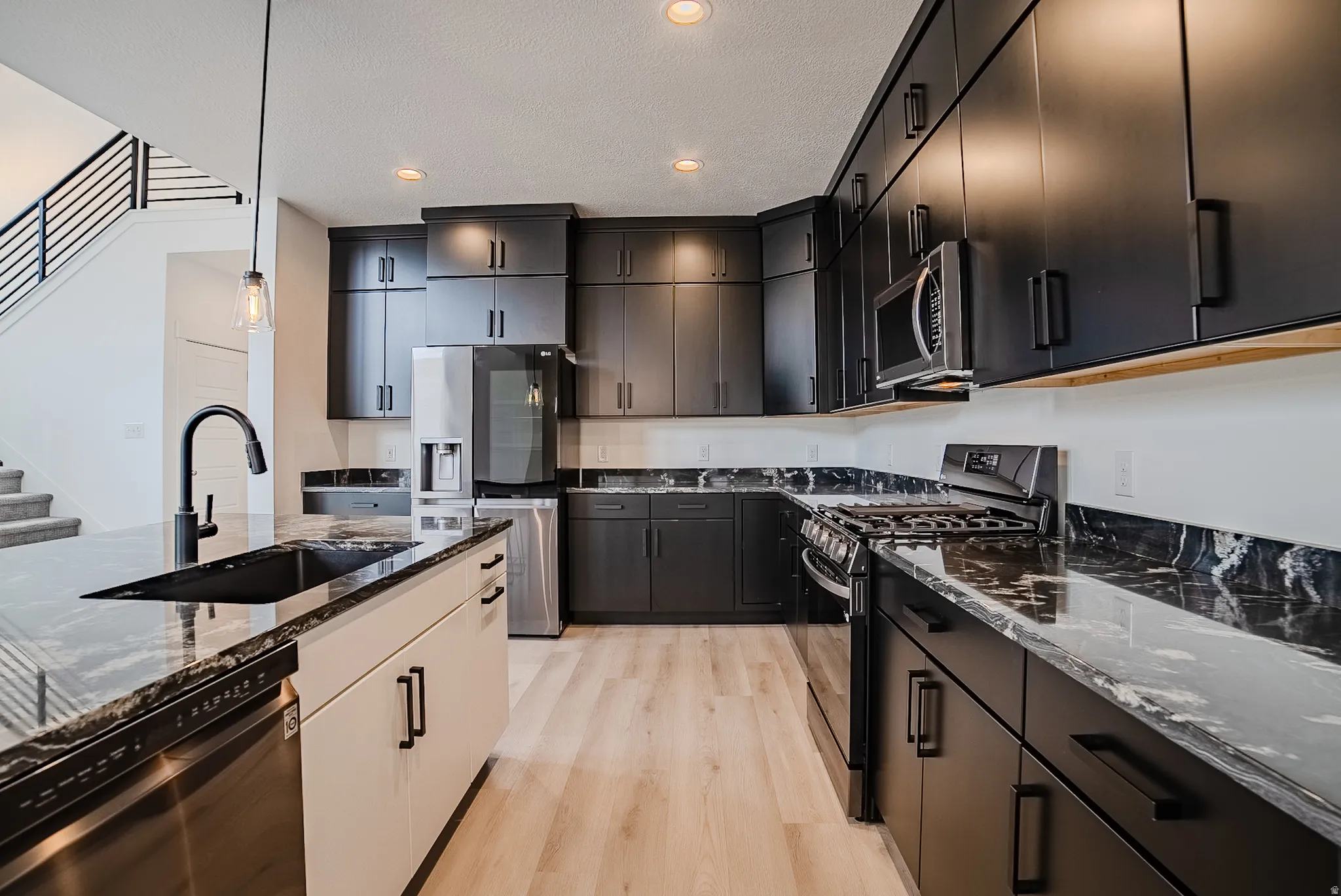 Modern kitchen featuring black cabinetry, light wood-finish flooring, and dark patterned countertops