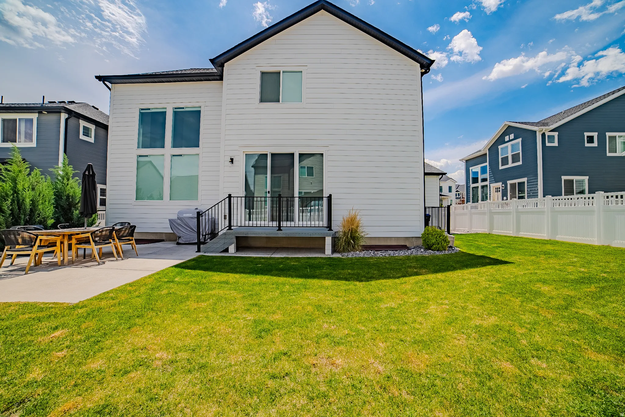 Expansive backyard featuring a manicured lawn, concrete patio, and a deck with metal railings