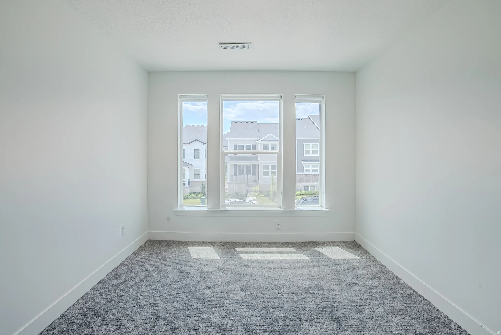 Bright room with three large windows, white walls, gray textured carpeting, and white baseboards