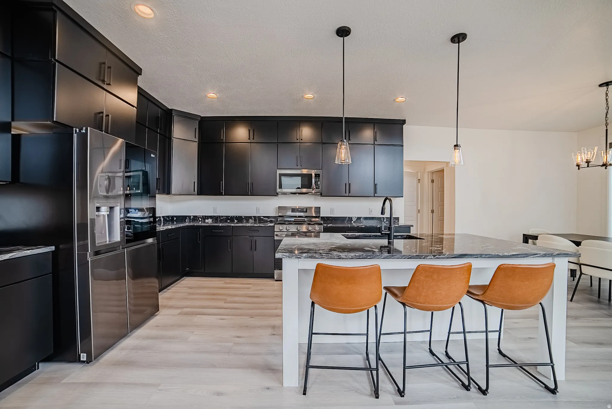 Spacious kitchen featuring extensive dark cabinetry, light wood-finish flooring, a generous center island with countertop seating, and recessed lighting