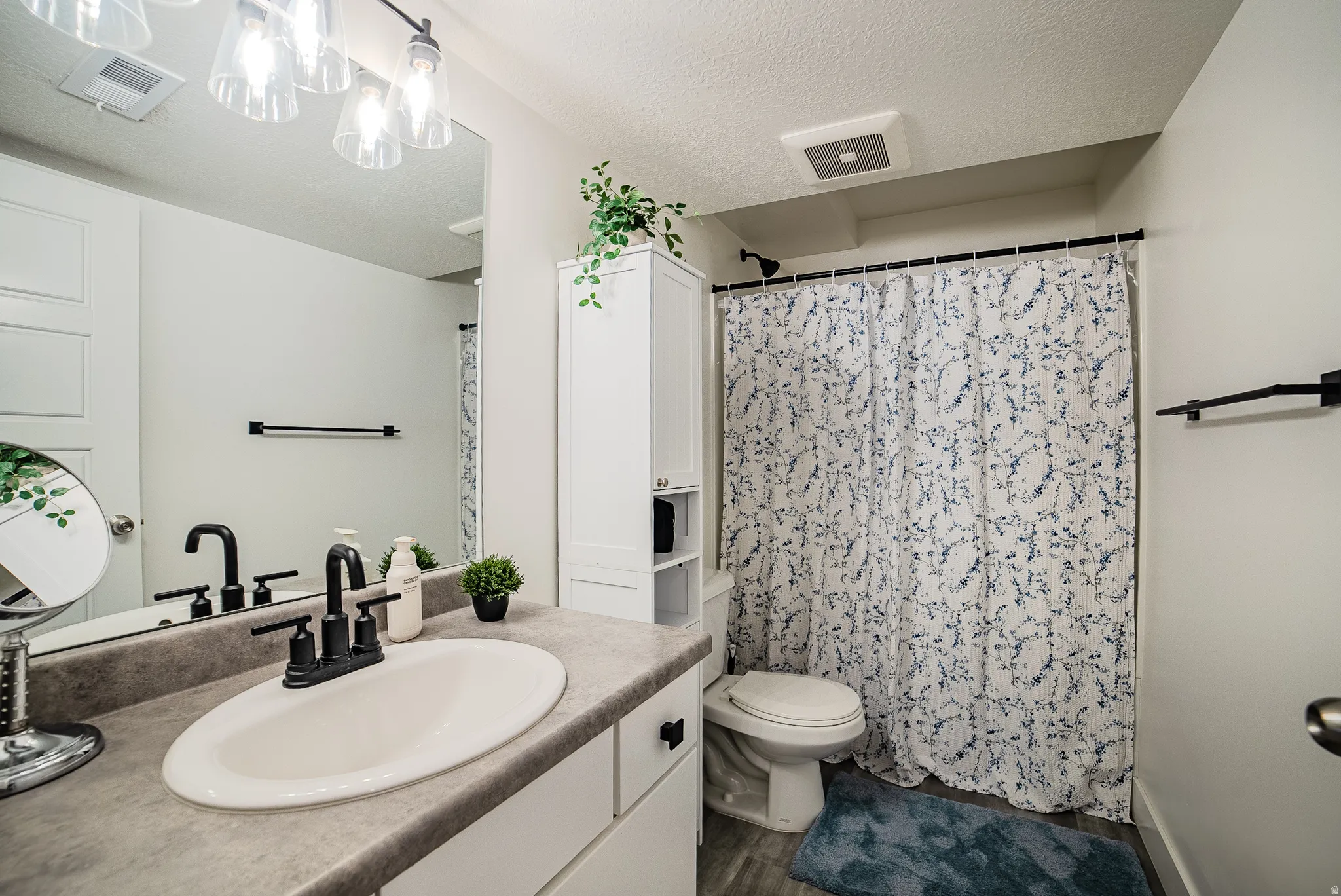 Bathroom featuring a single vanity with an oval sink and dark gray countertop, white cabinetry with black hardware, and a black faucet