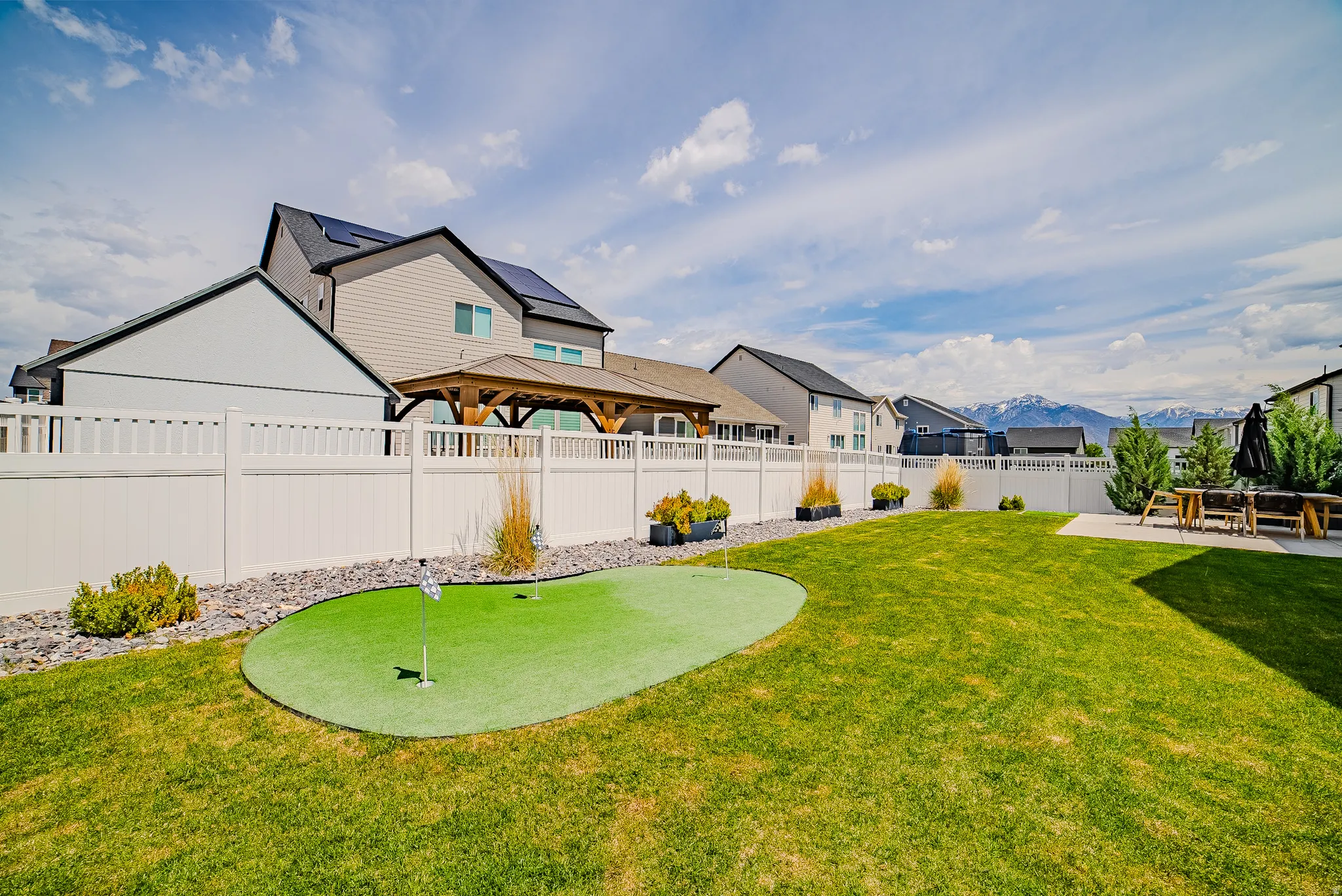 Expansive backyard featuring a green lawn, artificial turf putting green, and a concrete patio