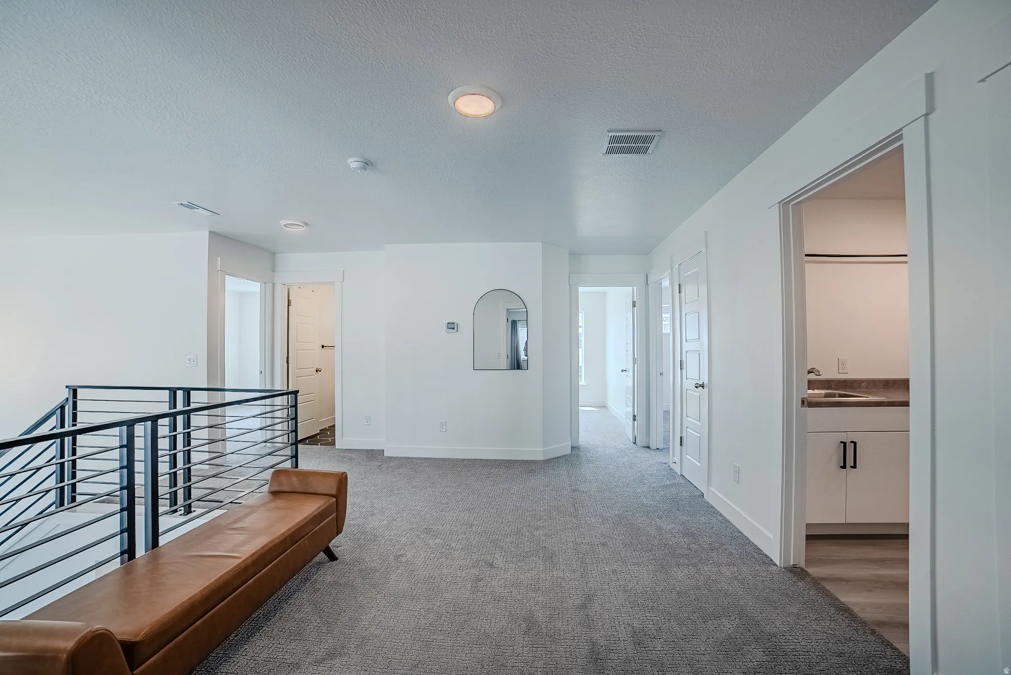 Spacious carpeted landing featuring a contemporary horizontal bar railing, recessed lighting, and crisp white walls