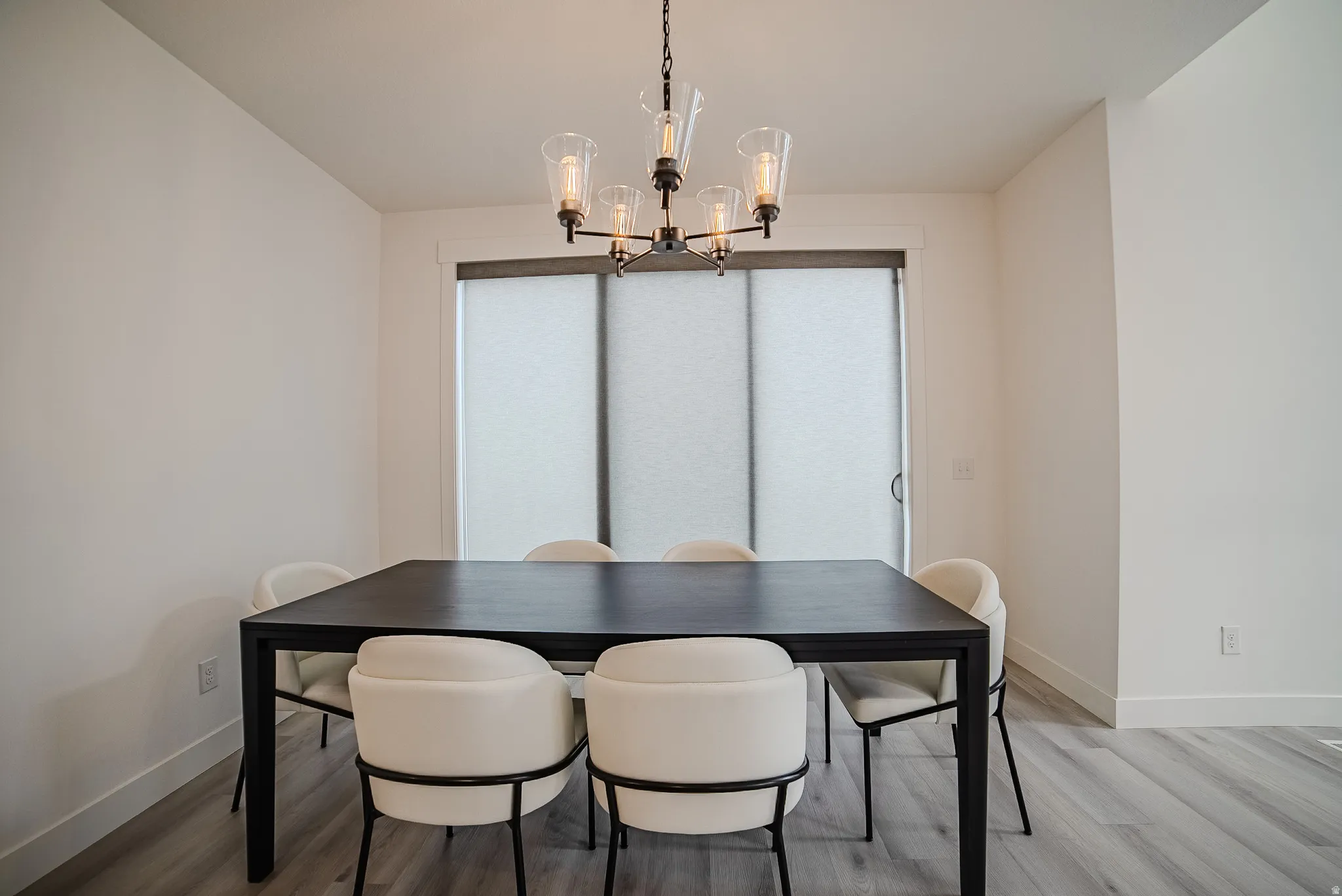 Dining area featuring a contemporary chandelier with clear glass shades, a sliding glass door with privacy blinds, and light wood-finish flooring