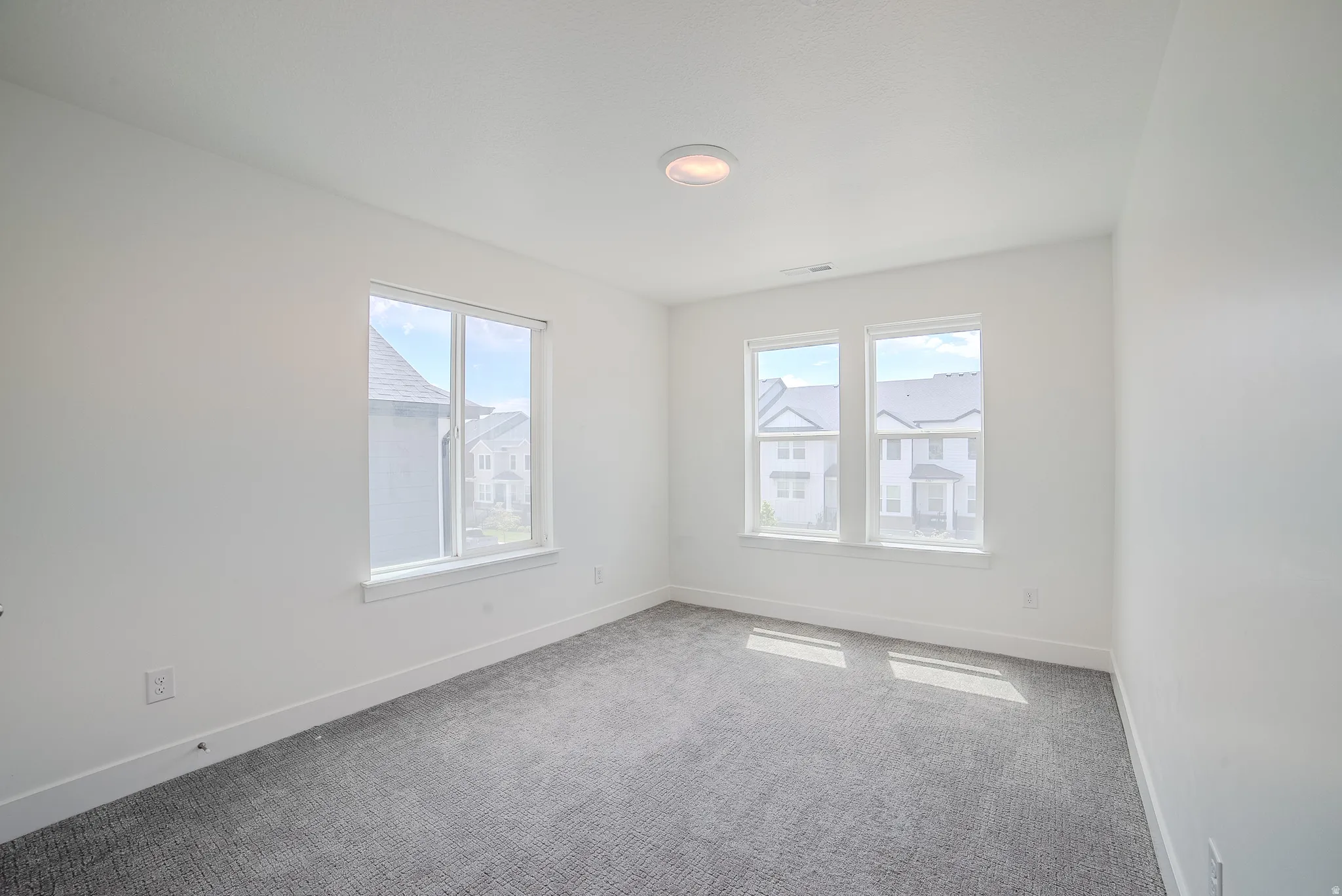 Room featuring white walls and trim, textured gray carpeting, and a flush-mount ceiling light