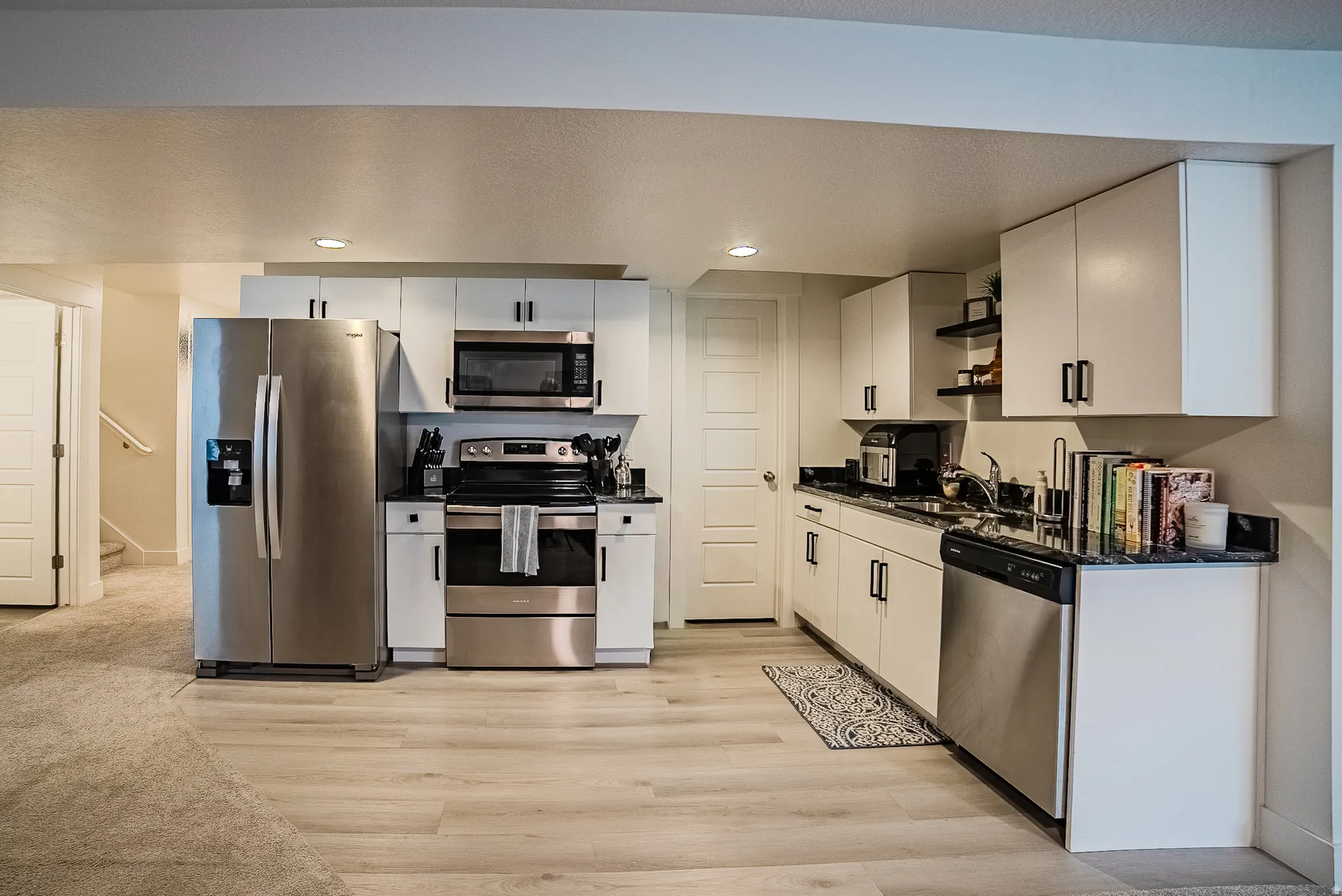 Modern kitchen featuring stainless steel appliances, white cabinetry with matte black hardware, dark countertops, and wood-finish flooring