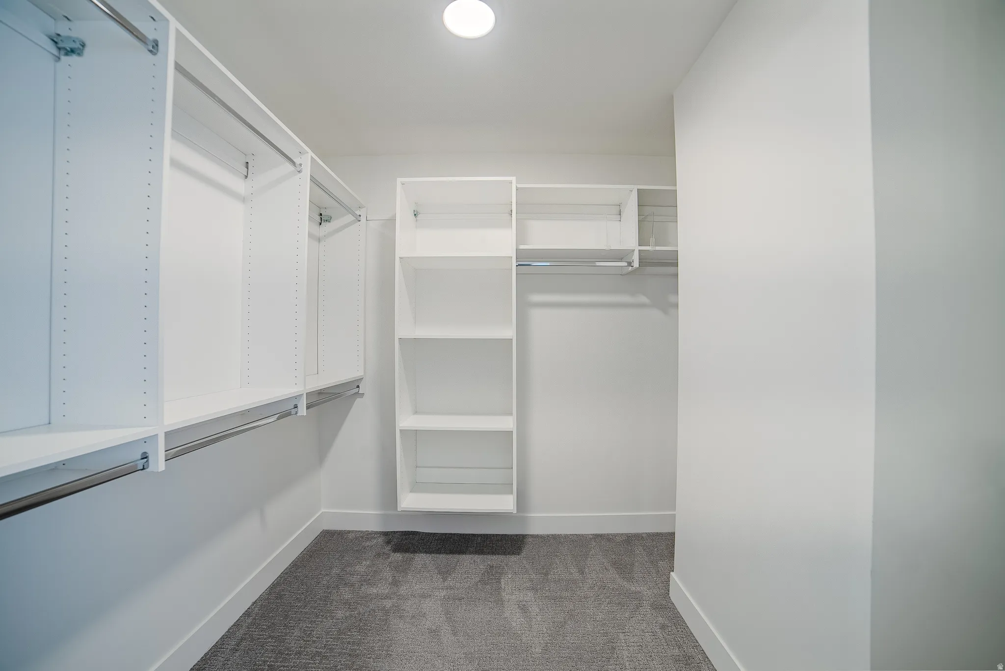 Walk-in closet featuring white built-in shelving, chrome hanging rods, recessed lighting, and gray carpeting