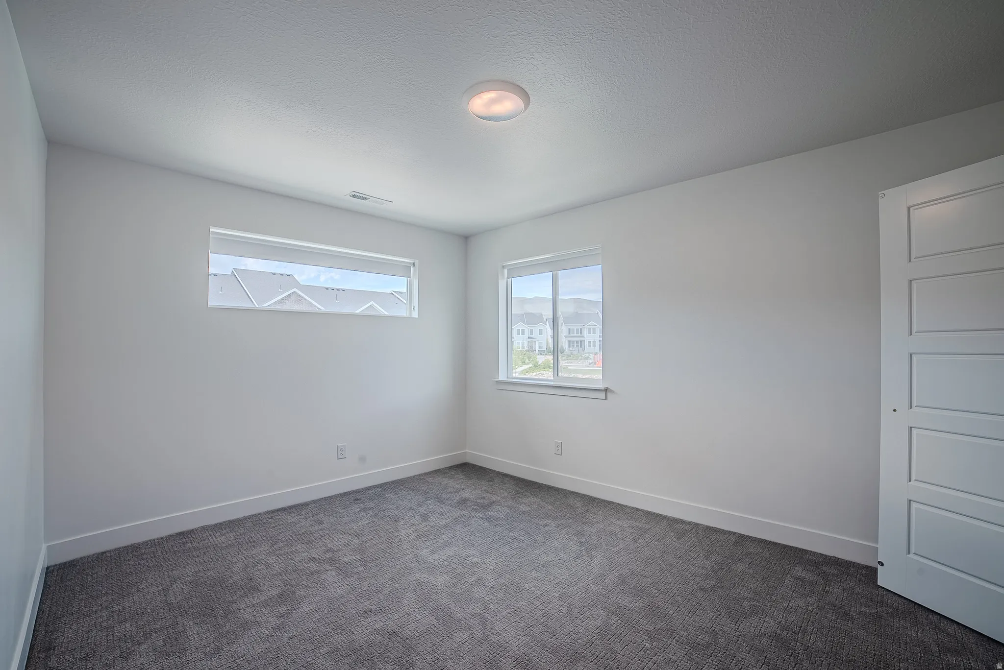 Carpeted room featuring a ceiling-mounted light fixture, white walls, and broad baseboards