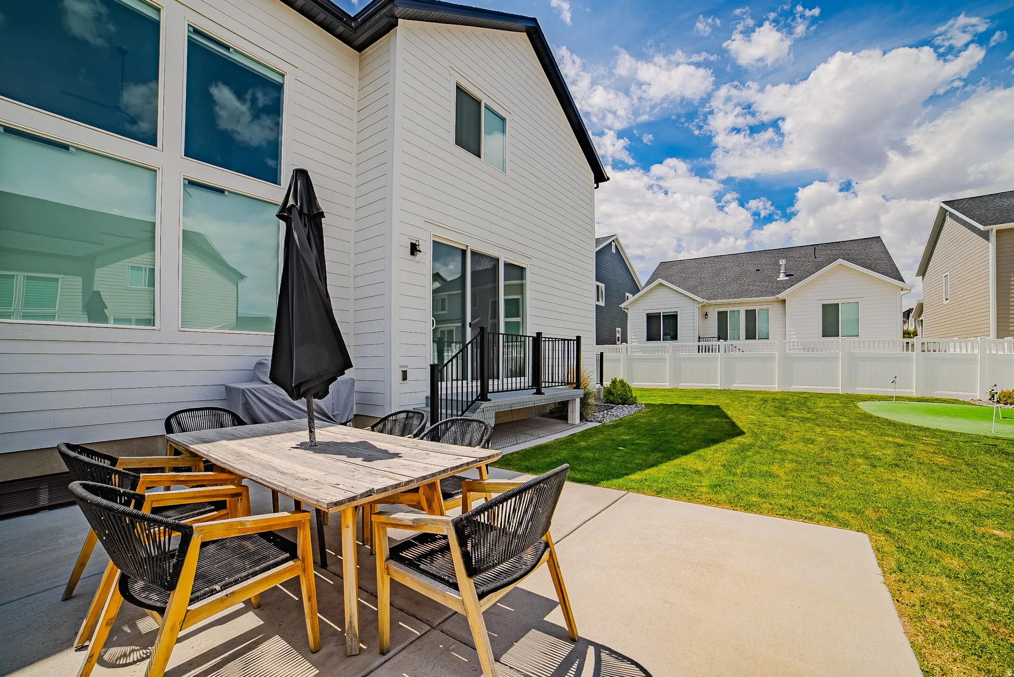 Expansive concrete patio with a spacious backyard featuring a putting green