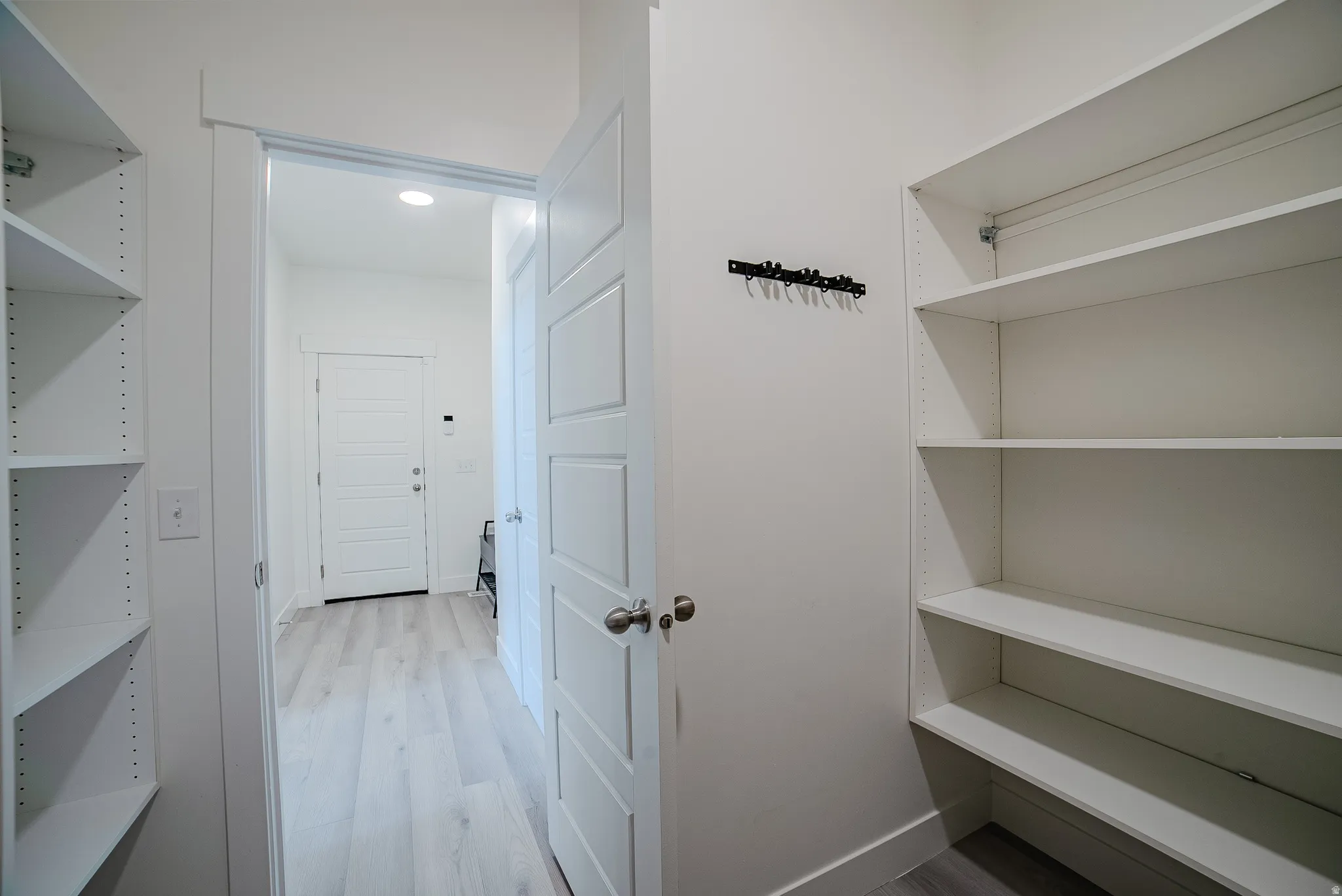 Dedicated pantry storage featuring adjustable shelving, light wood-finish flooring, recessed lighting, and a paneled interior door