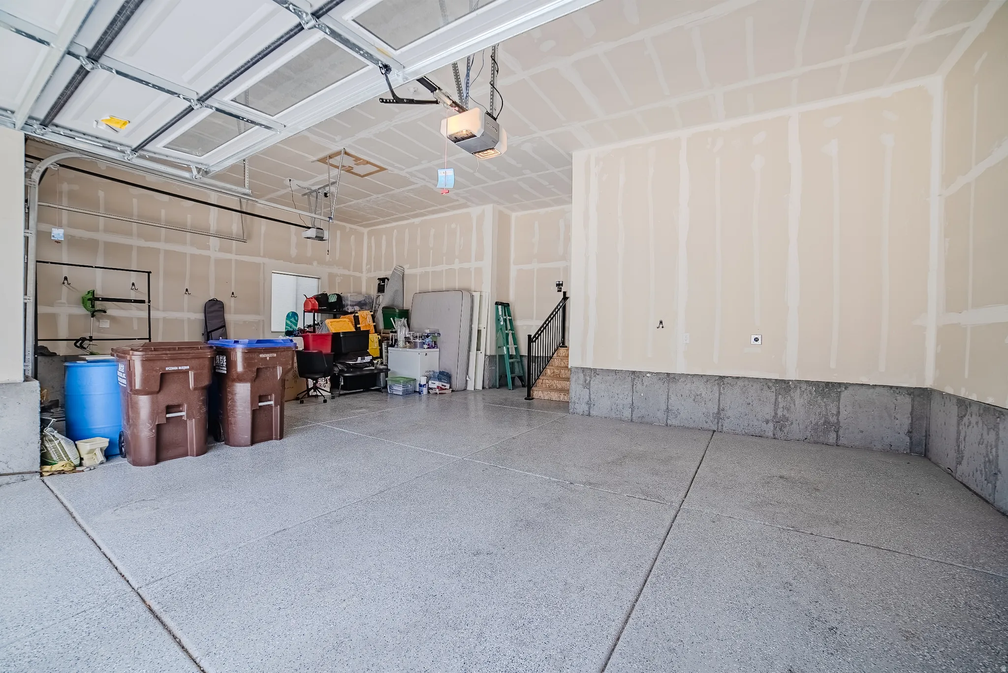 Spacious garage featuring an epoxy-coated concrete floor, an overhead door with an opener, and a staircase with a metal handrail