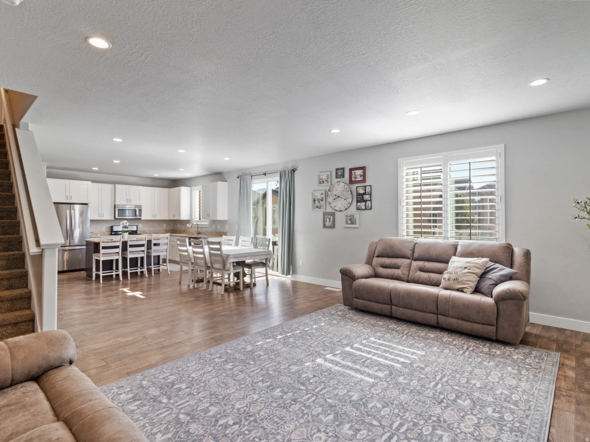 Open-concept living area featuring wood-finish flooring, recessed lighting, and a window with plantation shutters