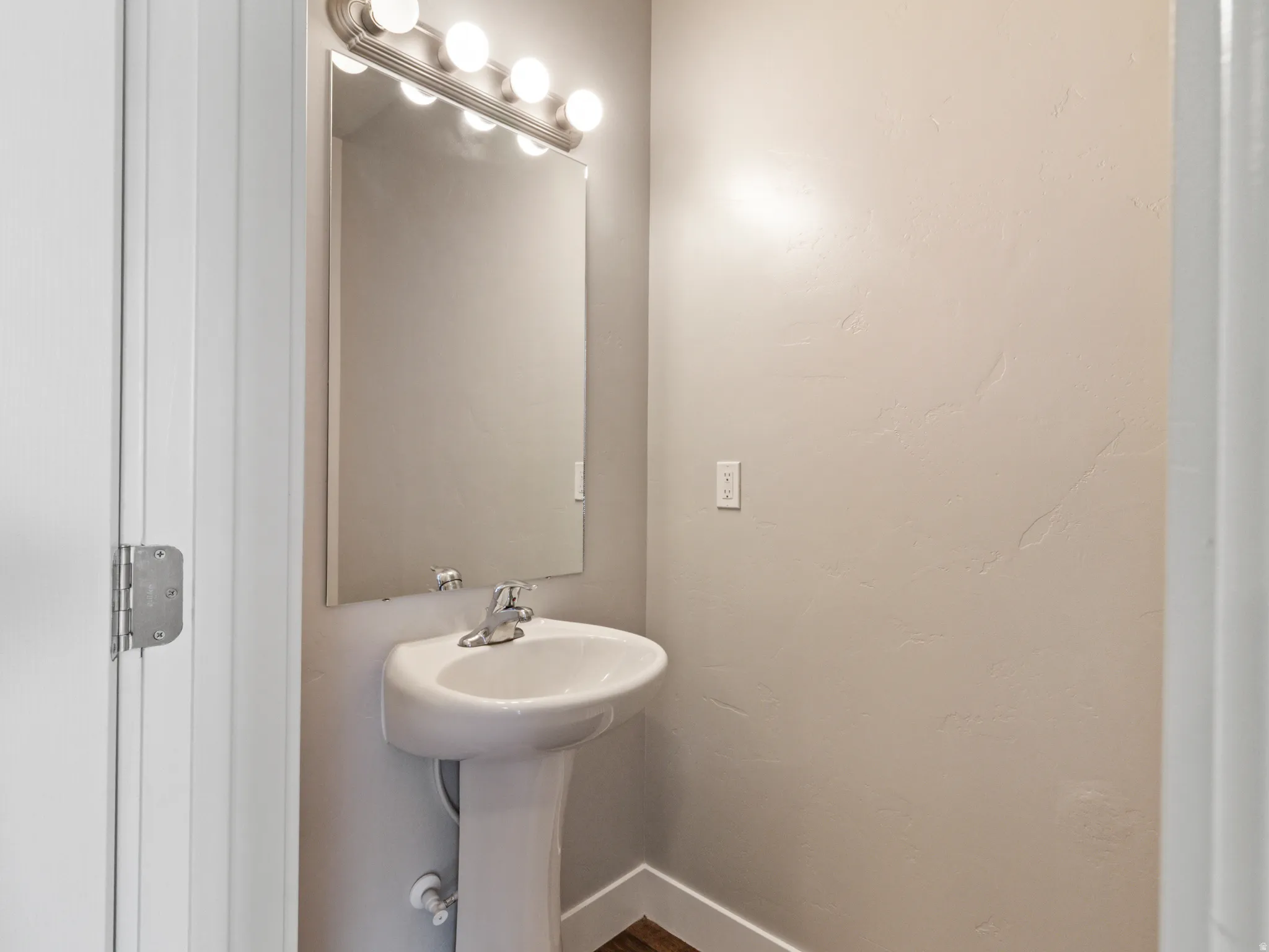 Pedestal sink with a chrome faucet, illuminated by a four-bulb vanity light fixture