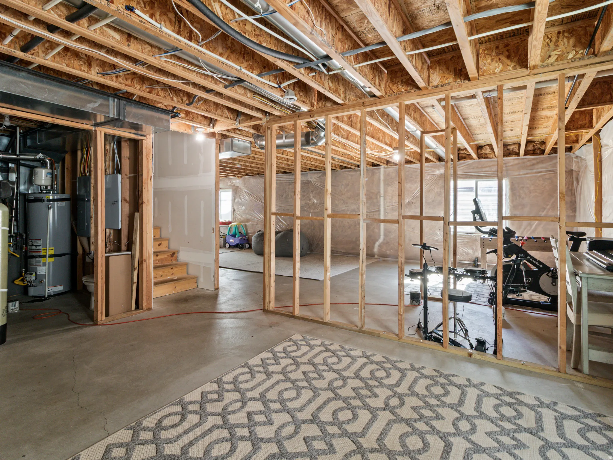 Unfinished basement featuring exposed wood framing, concrete flooring, and visible utility infrastructure, including a water heater