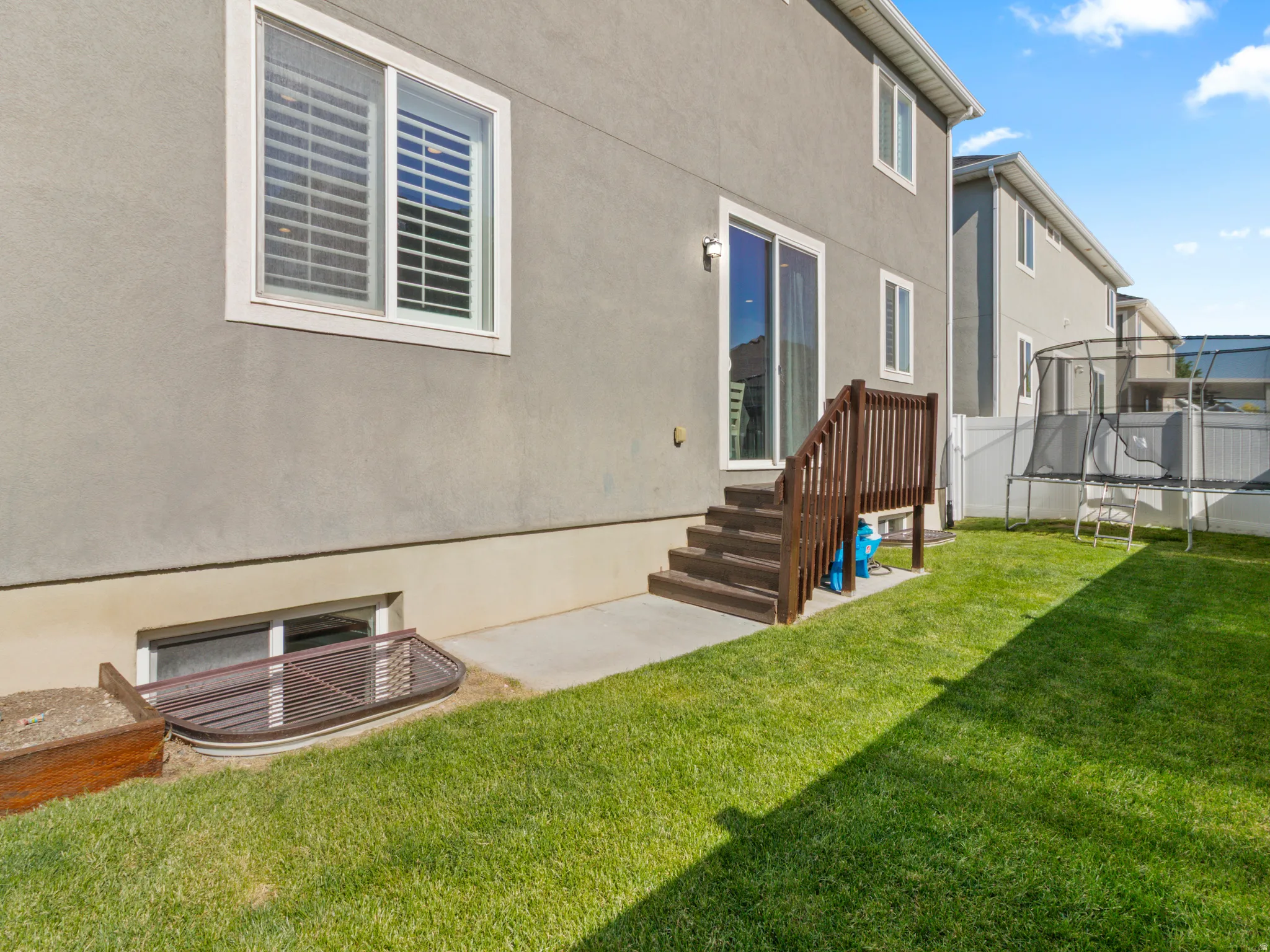 Expansive green lawn with concrete patio, leading to a wooden deck with stairs