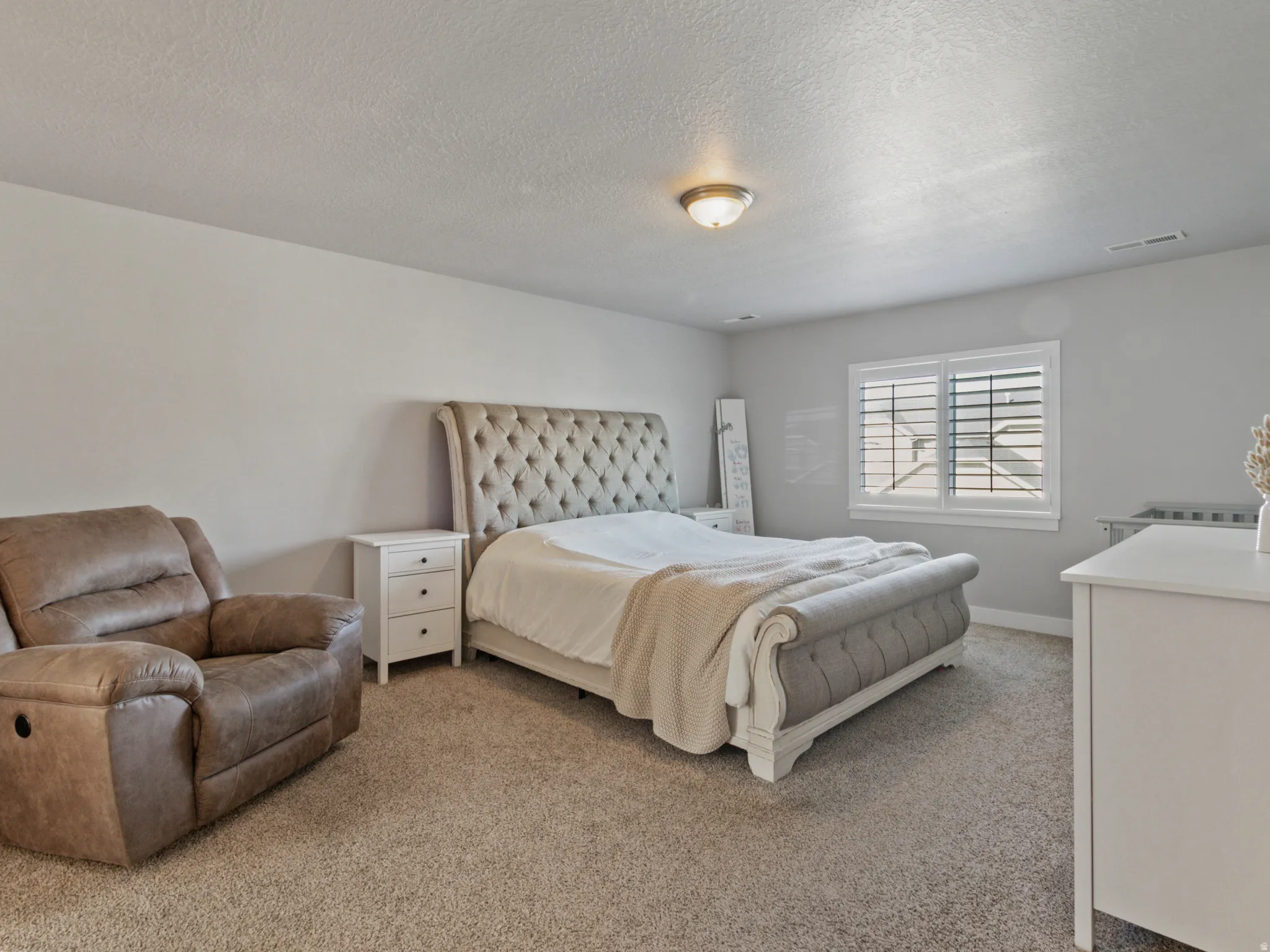 Wall-to-wall carpeted bedroom featuring a window with white plantation shutters, a ceiling-mounted light fixture, and light-toned walls