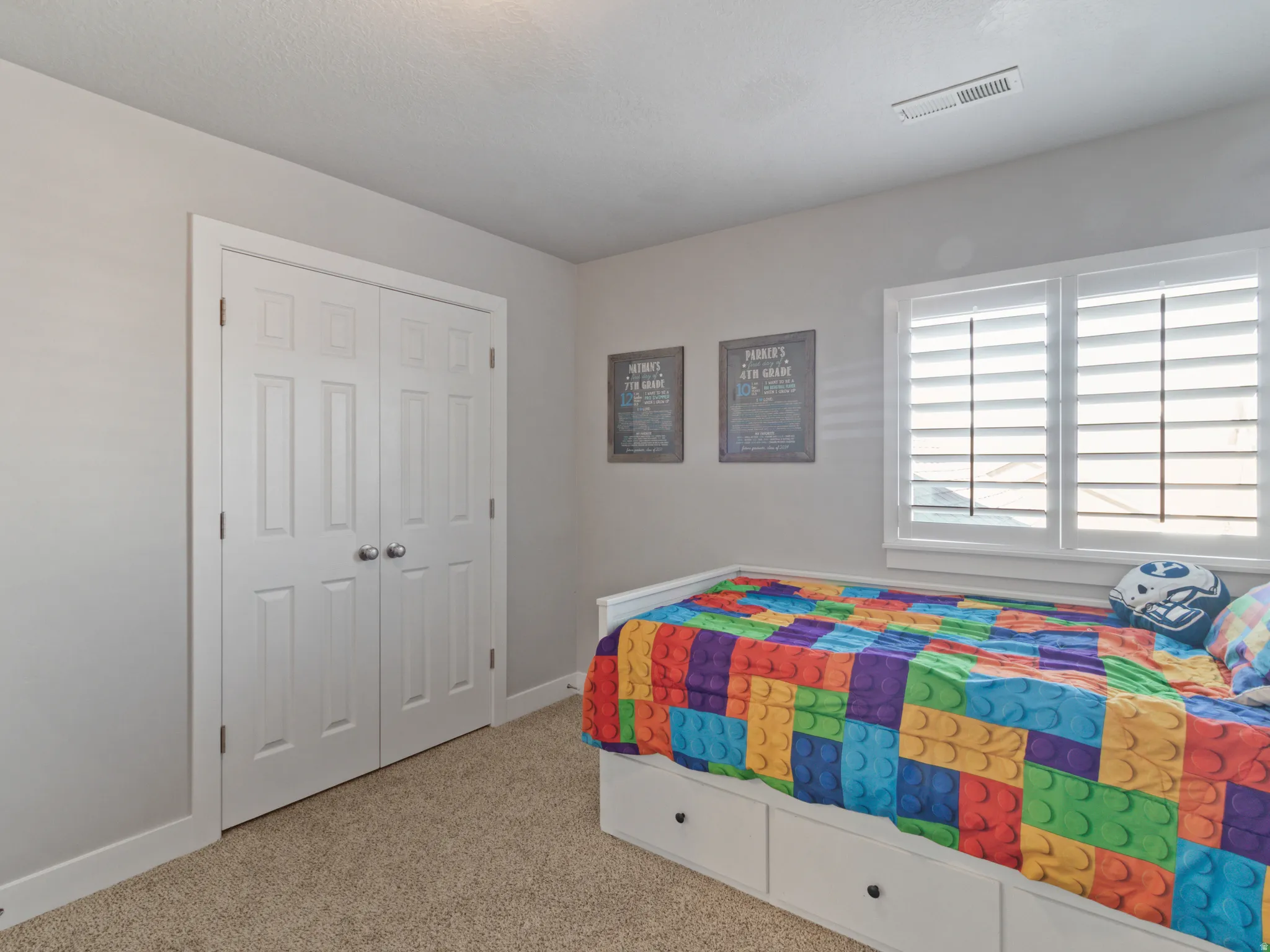 Bedroom featuring twin bi-fold closet doors, wall-mounted window shutters, and plush carpet flooring
