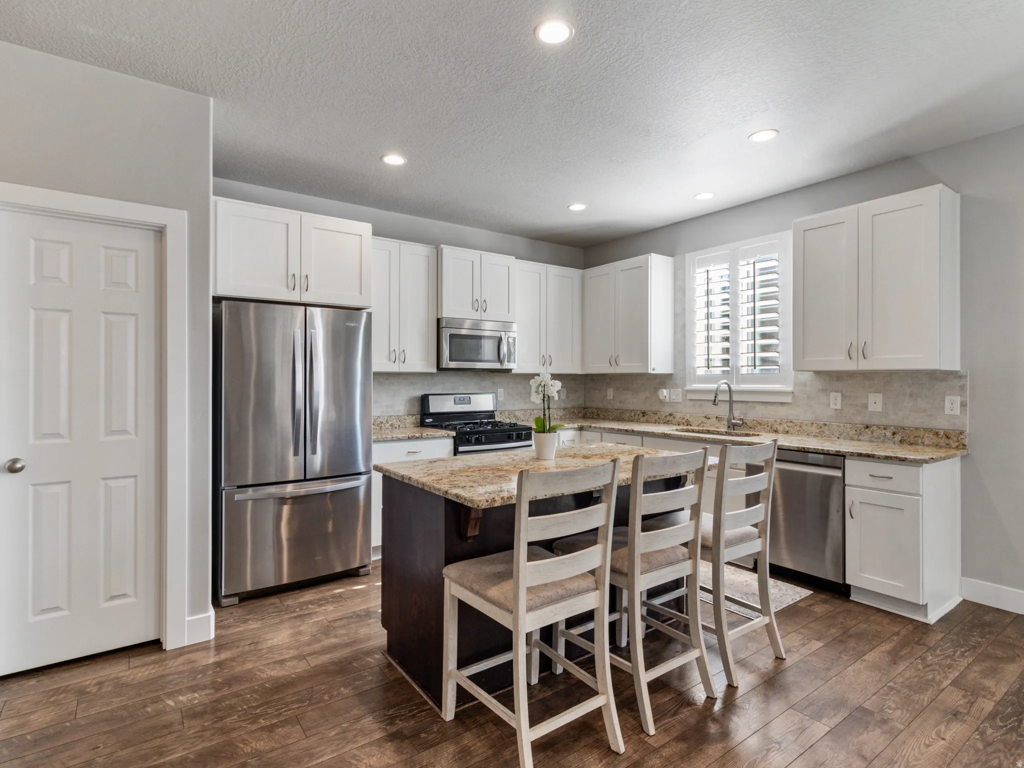 Modern kitchen featuring white shaker cabinetry, stainless steel appliances, a center island with seating, granite countertops, and wood-finish flooring