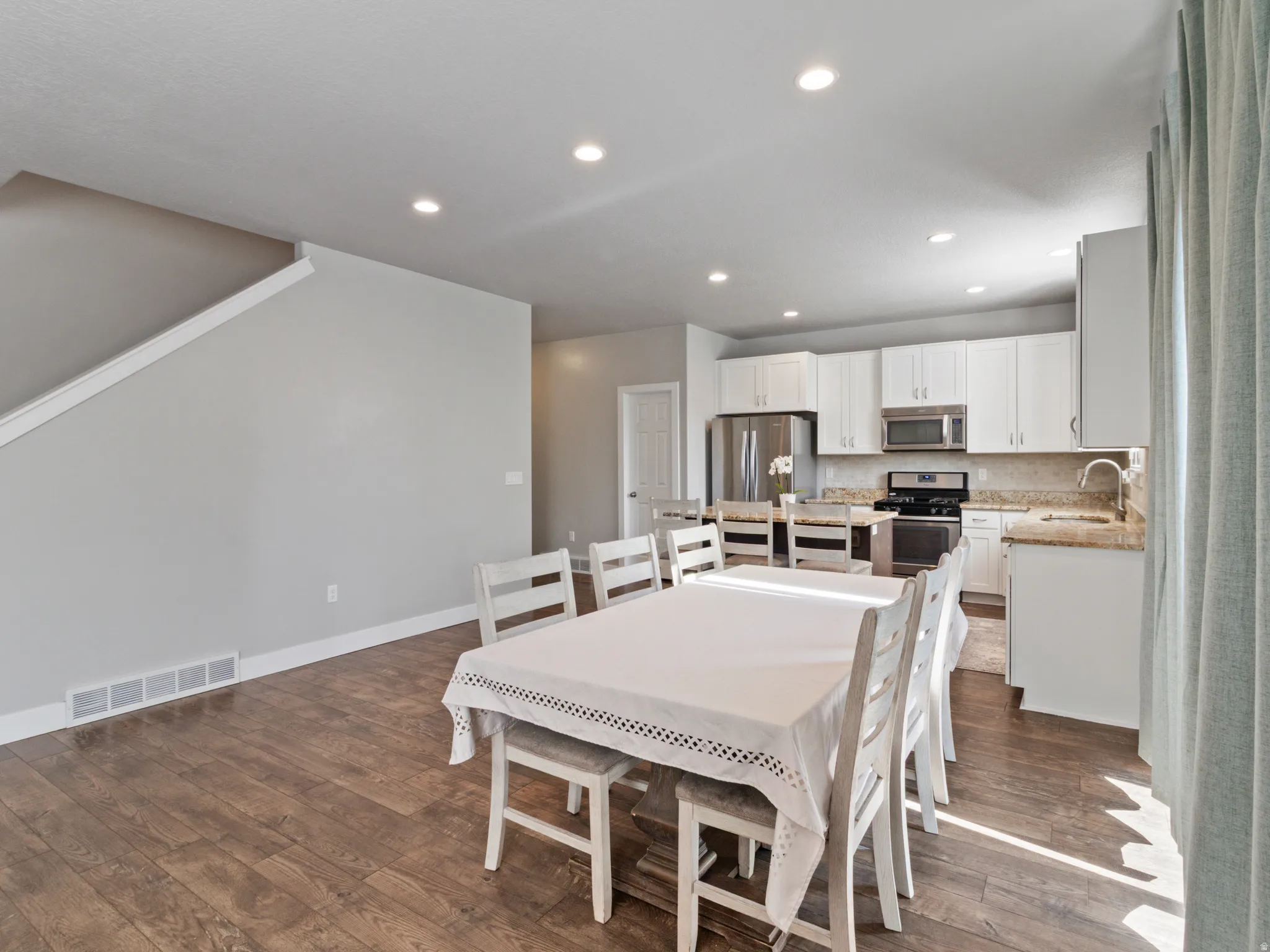 Open-concept living space featuring wood-finish flooring, recessed lighting, and a white kitchen with stainless steel appliances