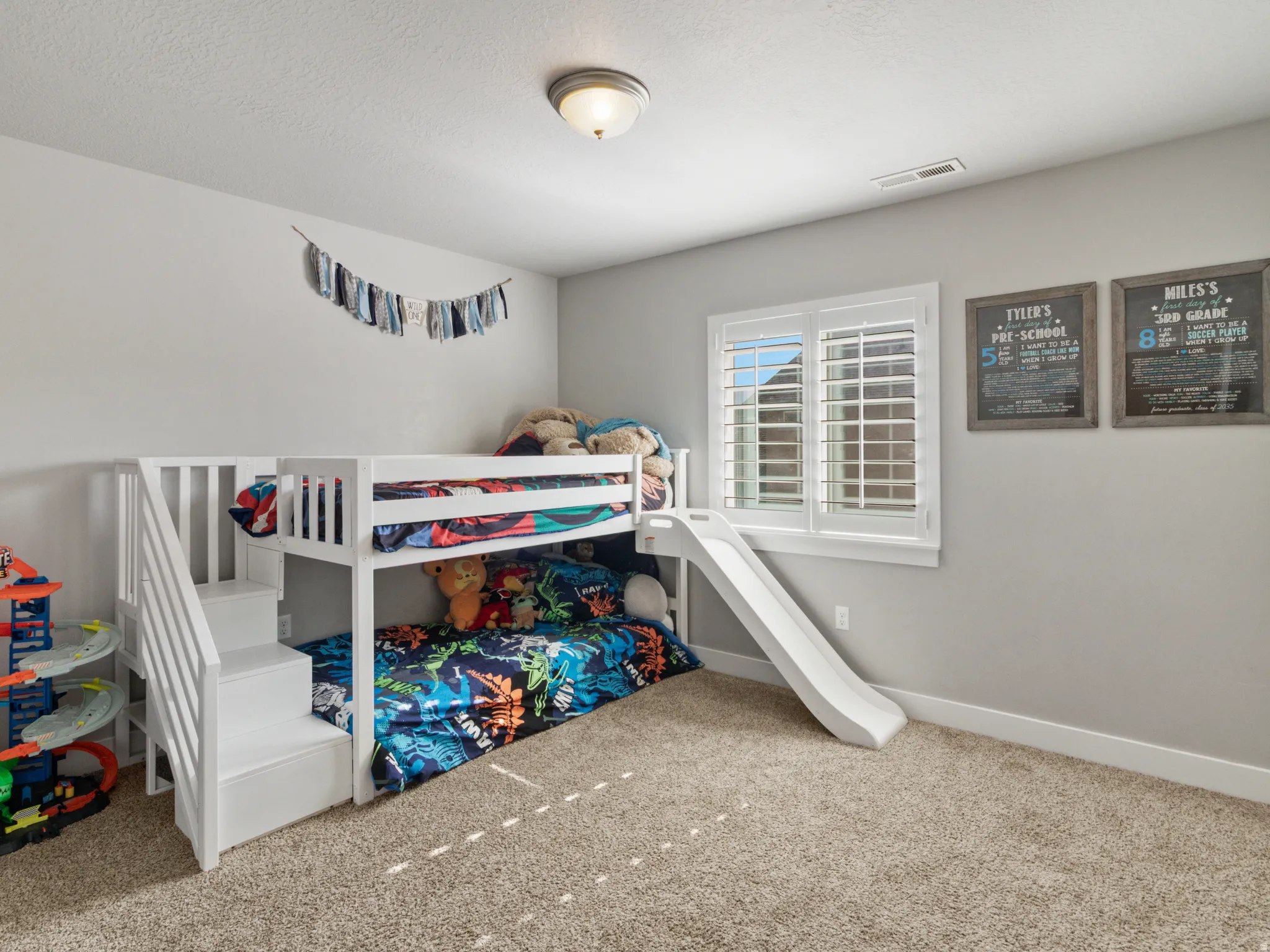 Carpeted room with a ceiling-mounted light fixture and a window featuring white plantation shutters