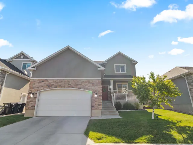 Contemporary exterior with stone veneer and stucco finishes, featuring an attached two-car garage, a covered front porch with white railings, and a well-maintained front lawn