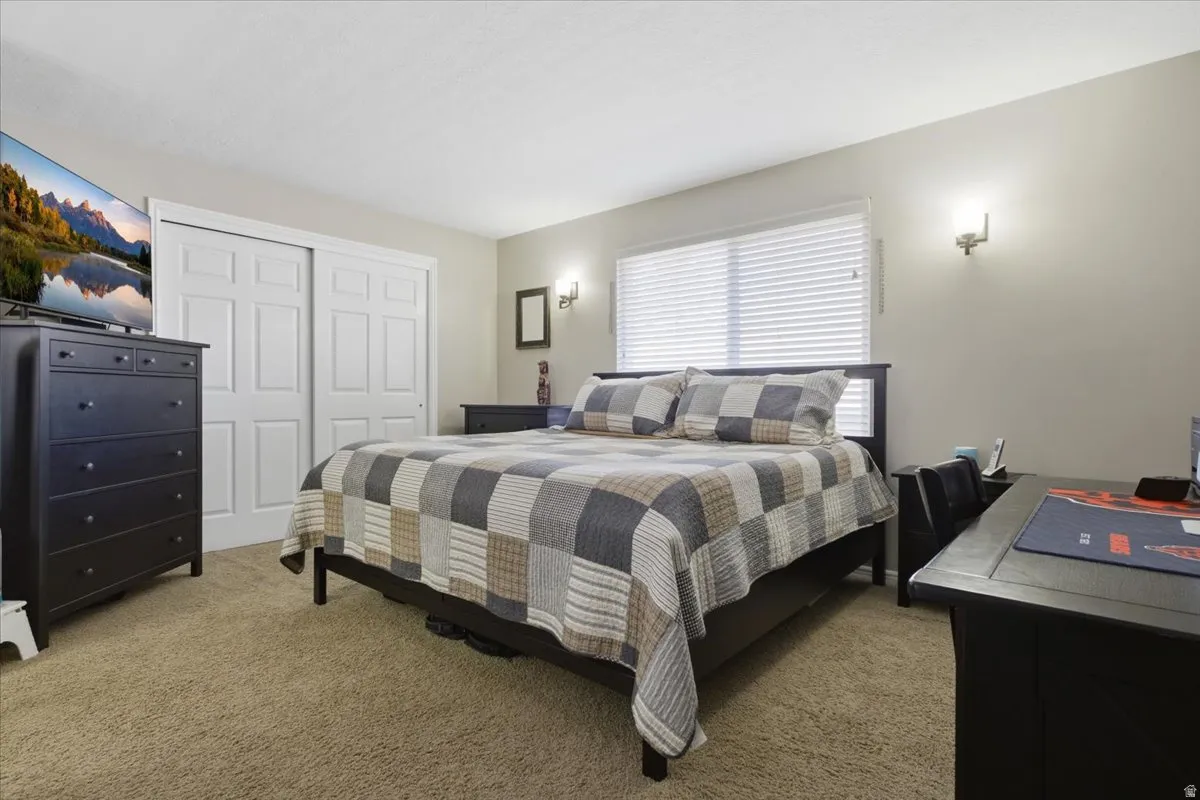 Carpeted room featuring a window with blinds, dual wall sconces, and built-in closet with sliding panel doors