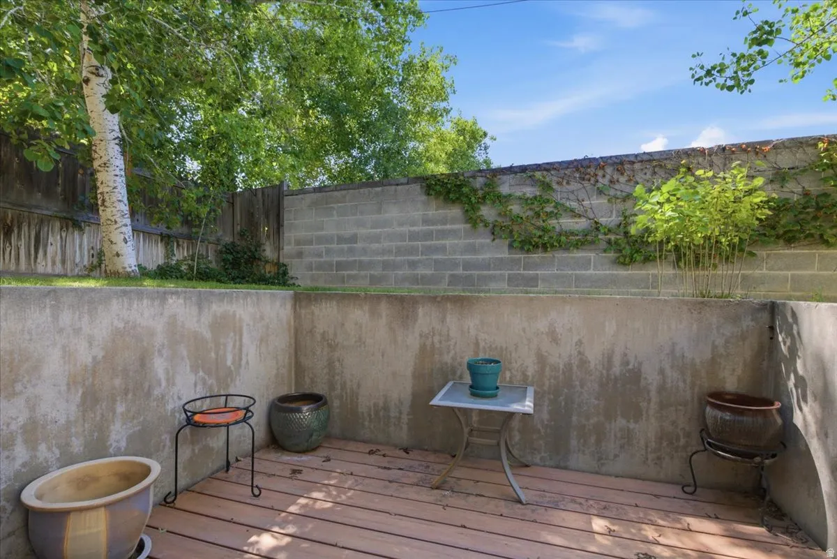 Private outdoor patio featuring wood-finish decking, concrete retaining walls, and a block perimeter wall with climbing greenery
