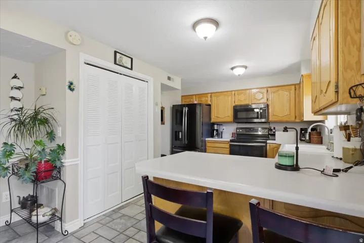 Kitchen featuring wood cabinetry, white countertops, black appliances, and gray tile flooring