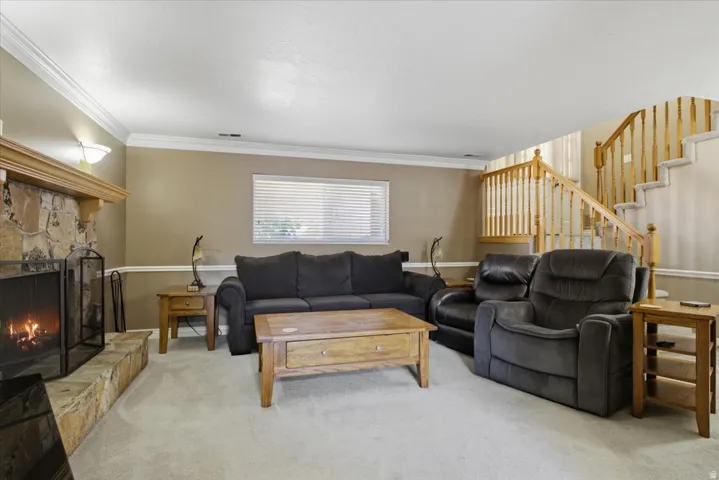 Living area featuring a stone fireplace with a wood mantle, soft carpet flooring, and a staircase with wood banisters