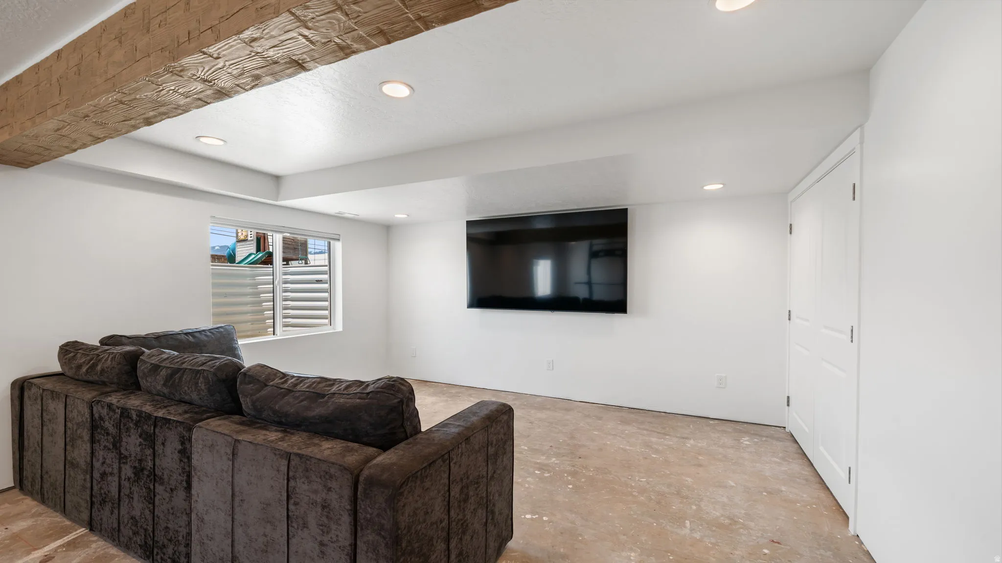 Recessed lighting illuminates this space featuring a mounted display, a window with horizontal blinds, and a white interior door