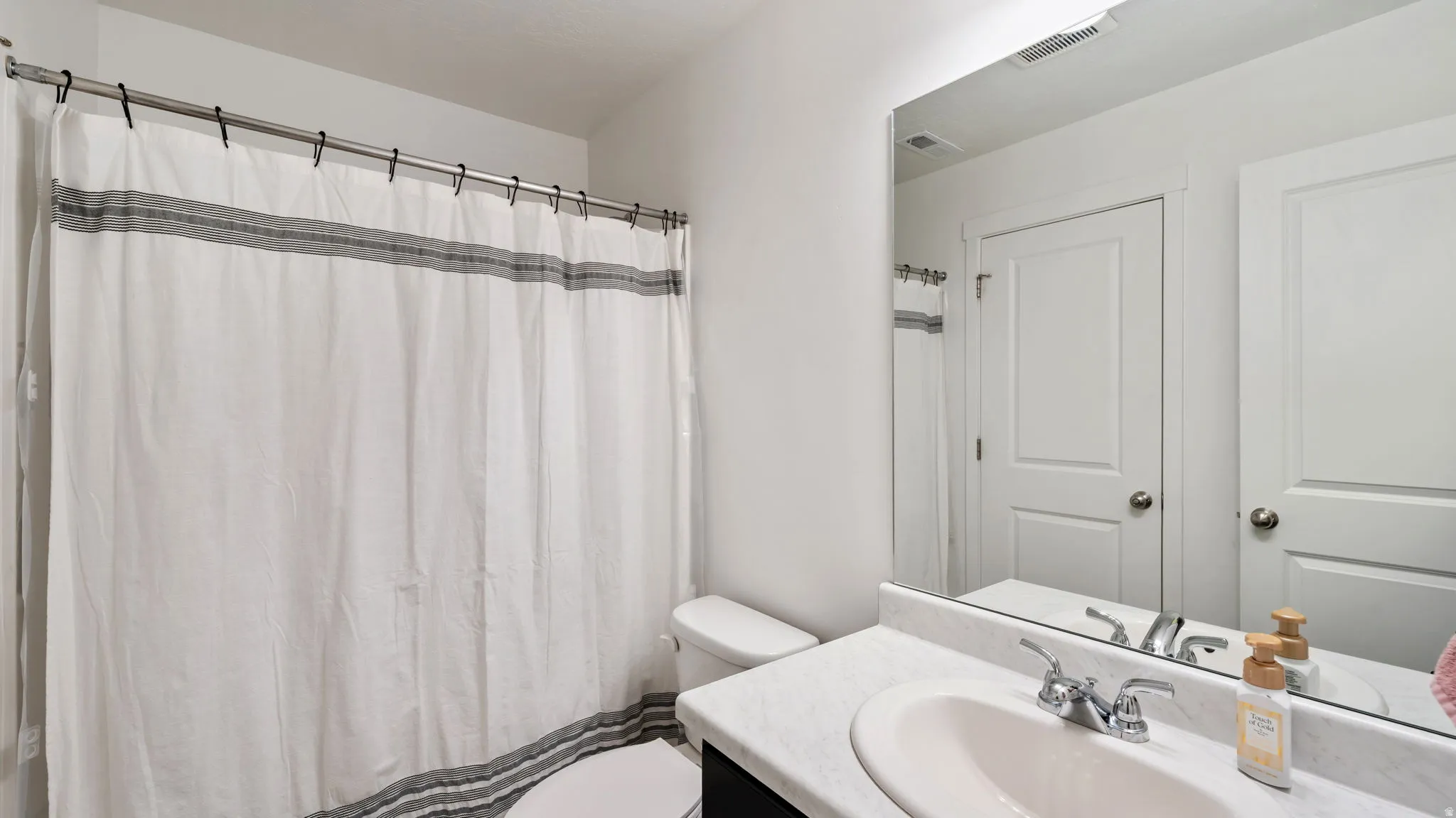 Bathroom featuring a shower with a curtain rod, a toilet, a vanity with an integrated sink, a chrome faucet, and a large wall-mounted mirror