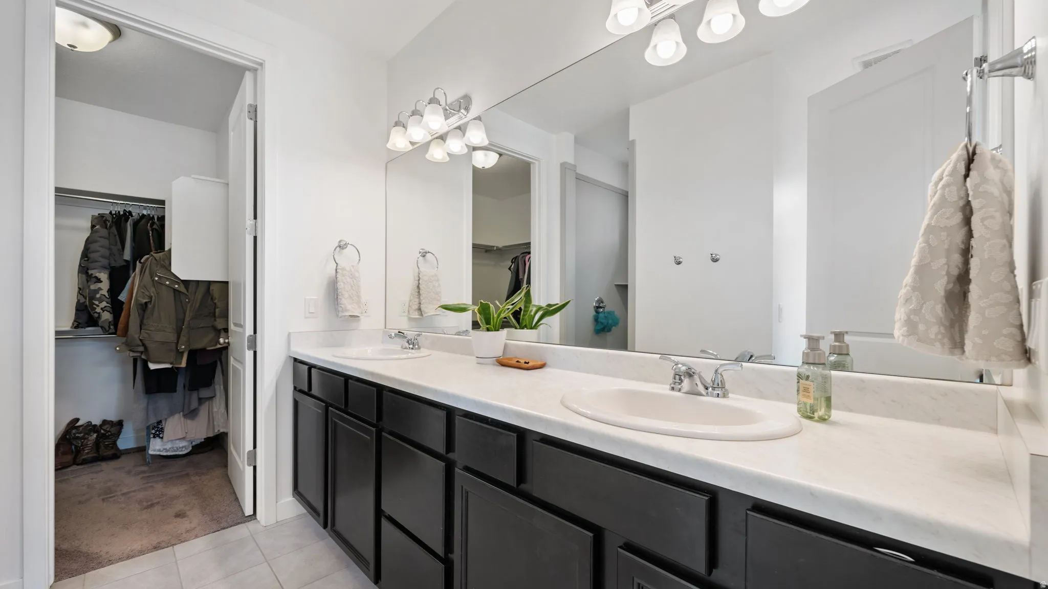 Master bathroom featuring a dual-sink vanity with dark cabinetry, ample counter space, a large wall mirror, and overhead vanity lighting