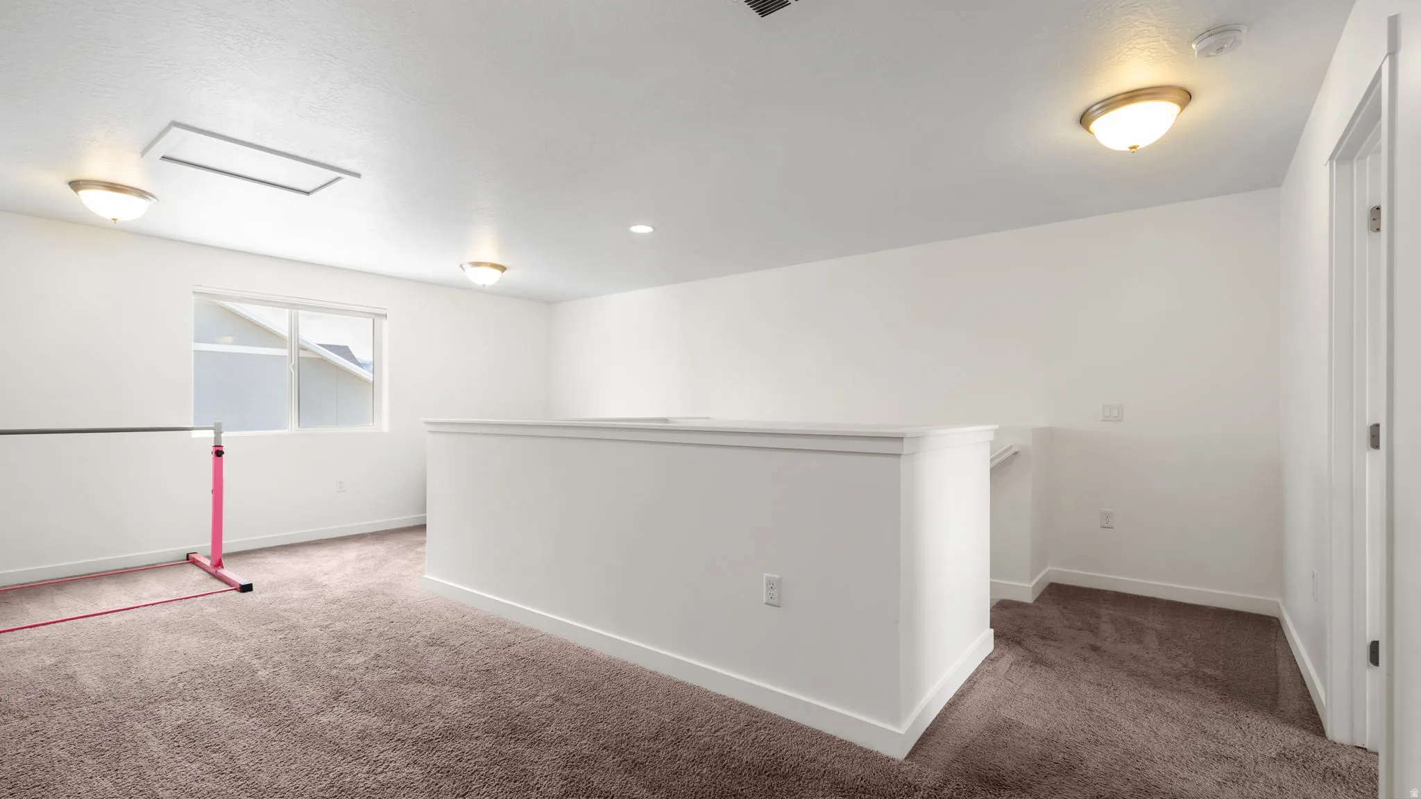 Carpeted loft area featuring a half-wall railing, recessed lighting, and a single window