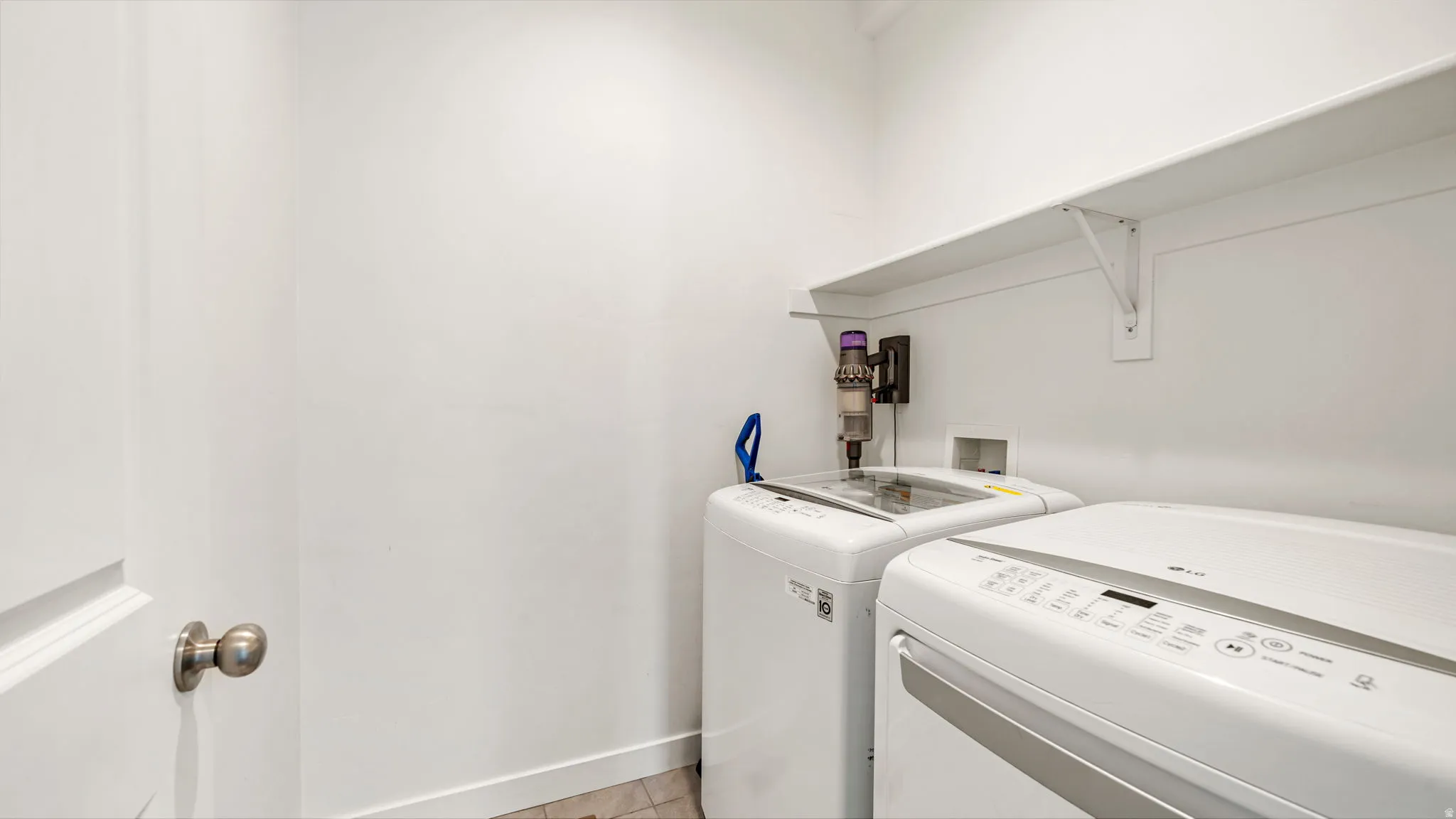Dedicated laundry area featuring white walls, a white storage shelf, and durable flooring