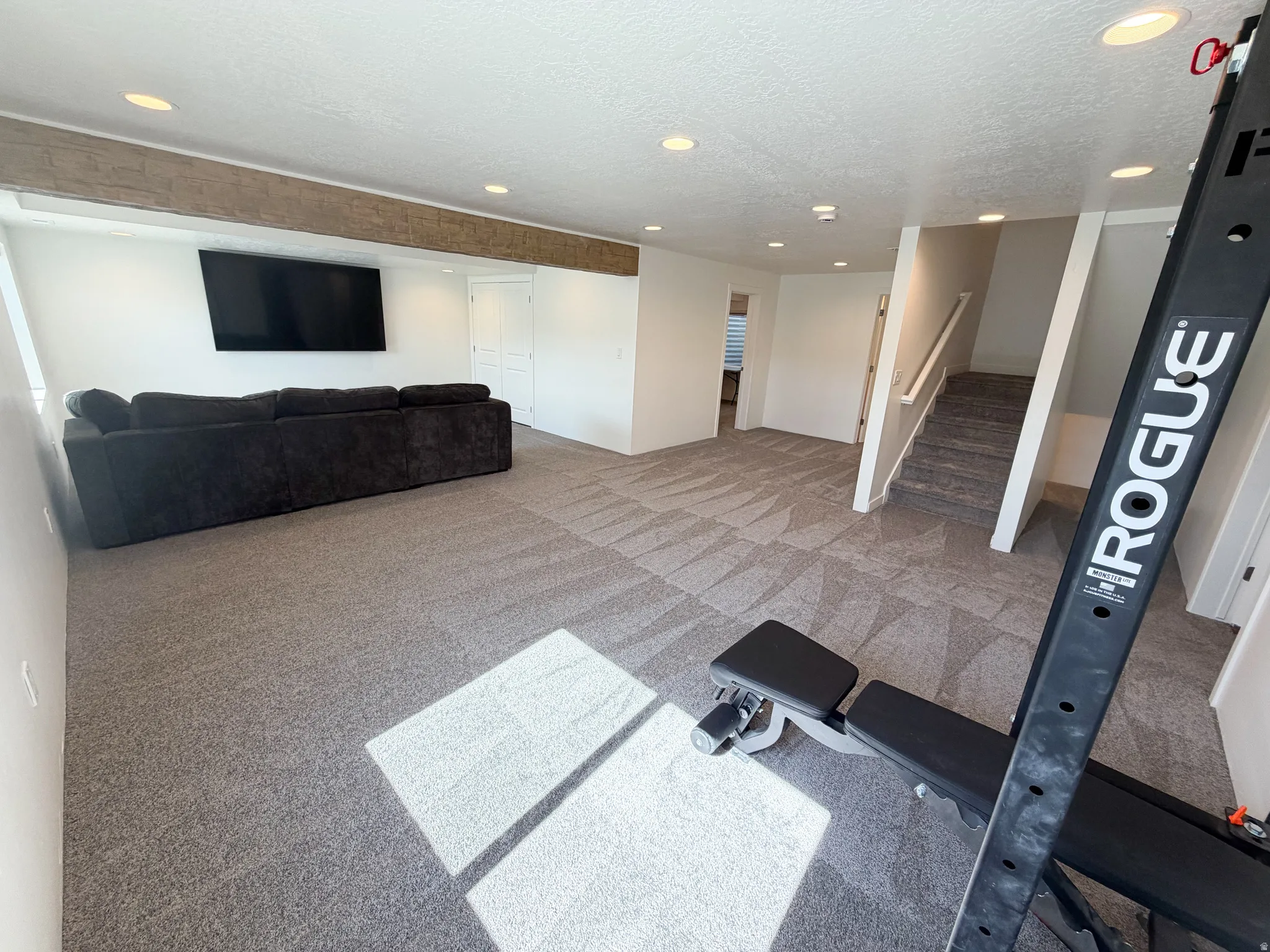 Open-concept lower-level recreation room with recessed lighting and a wood-finish ceiling beam
