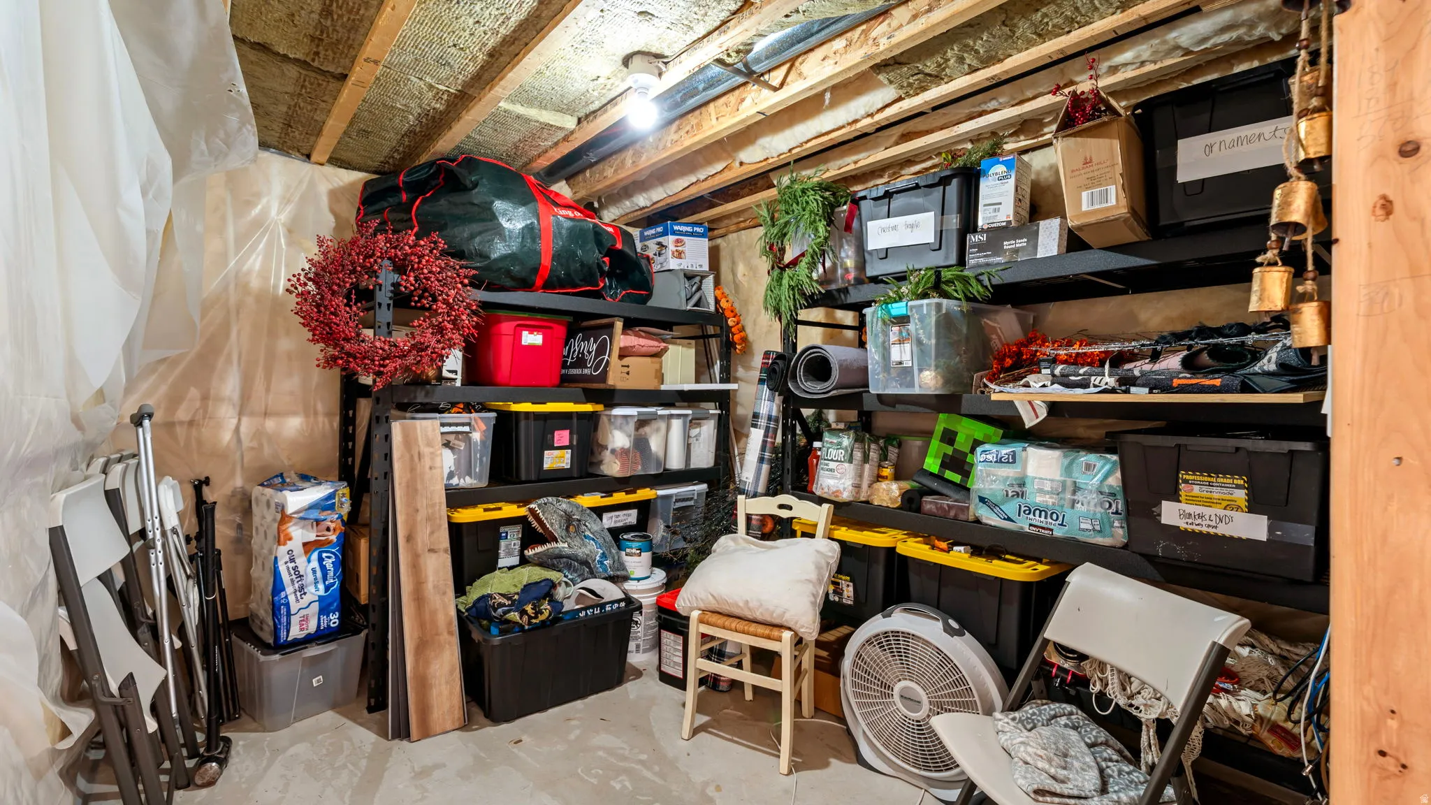 Unfinished basement space featuring exposed wooden ceiling joists, insulation, and an overhead light fixture