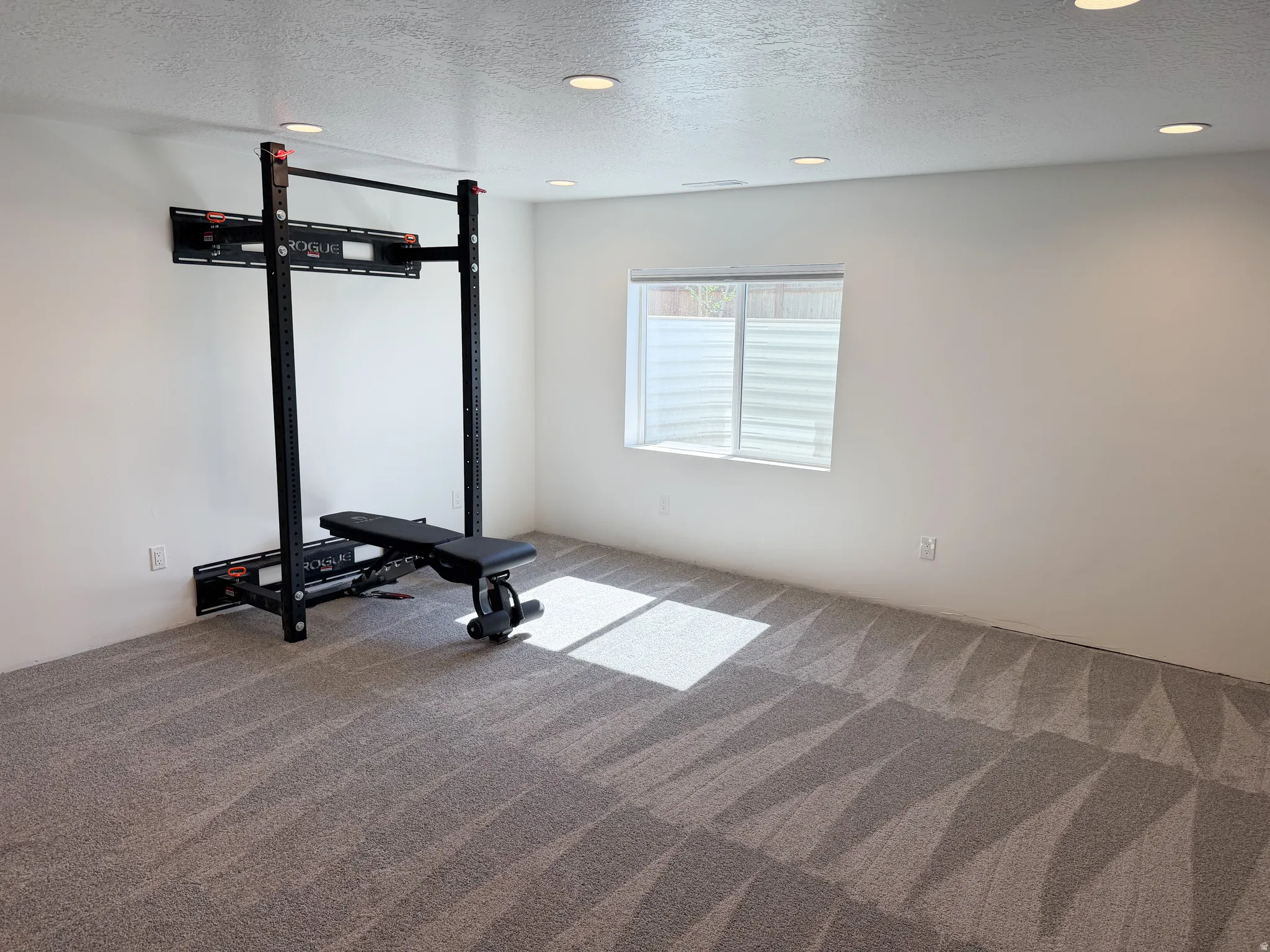 Spacious recreational area featuring recessed lighting, a window with horizontal blinds, and a durable concrete floor
