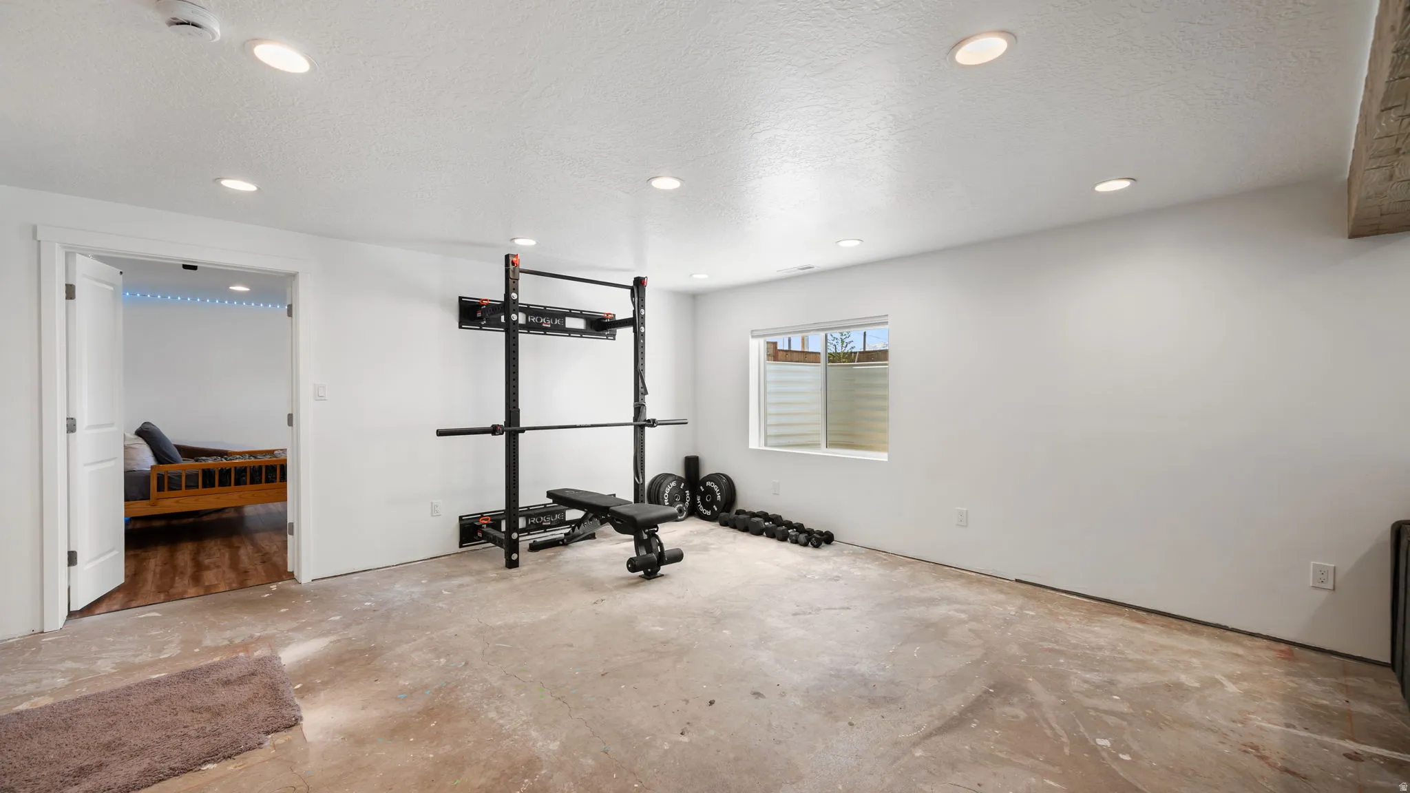 Spacious recreational area featuring recessed lighting, a window with horizontal blinds, and a durable concrete floor