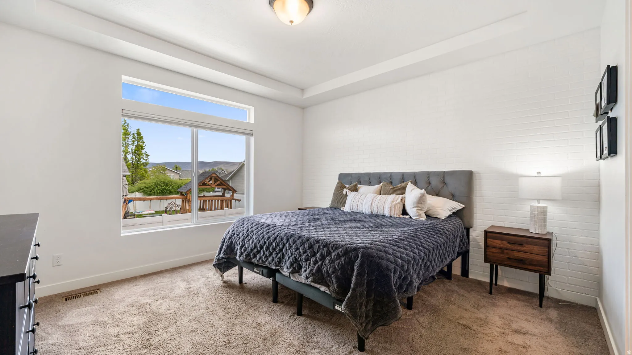 Spacious master bedroom featuring a large window with transom, tray ceiling, textured accent wall, and plush carpeting